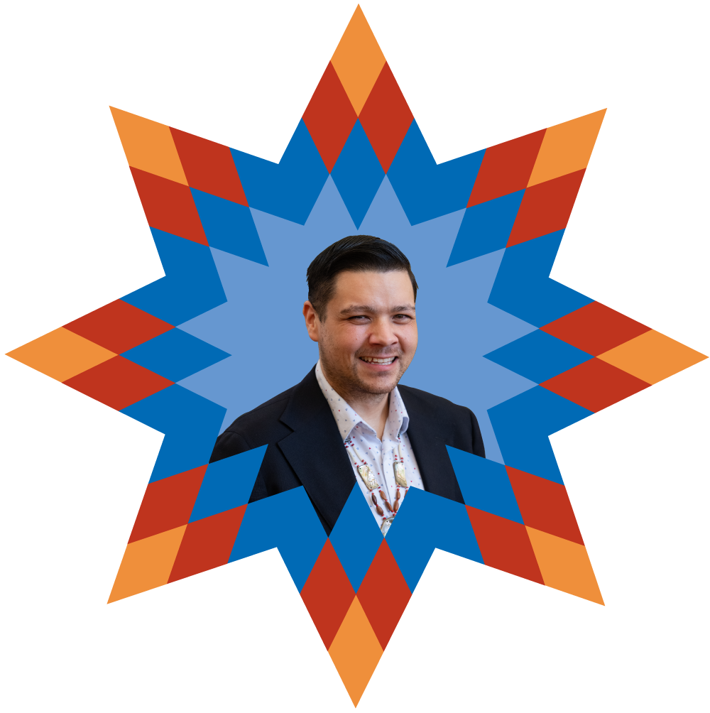 A smiling man in a suit jacket and patterned shirt is surrounded by a geometric, colorful starburst pattern in shades of blue, orange, and red.