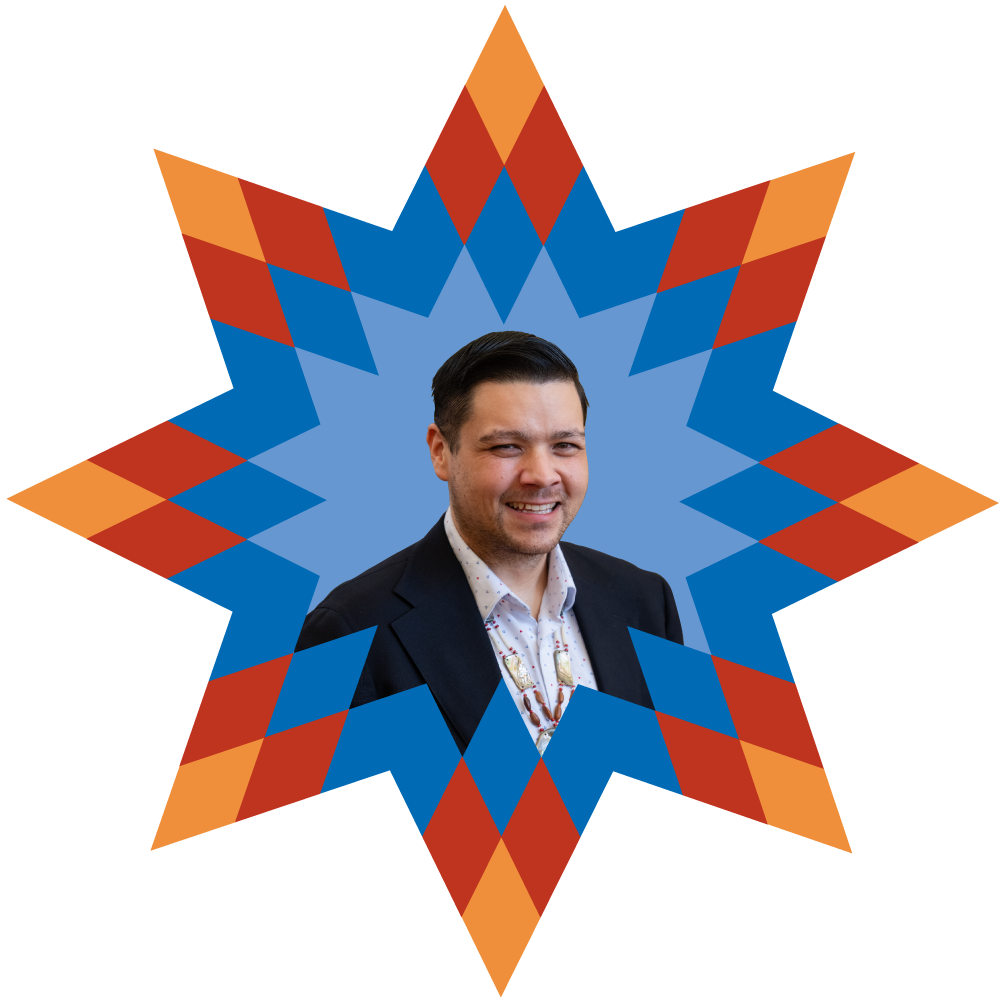 A man smiling in front of a geometric, starburst background in red, blue, and orange colors.