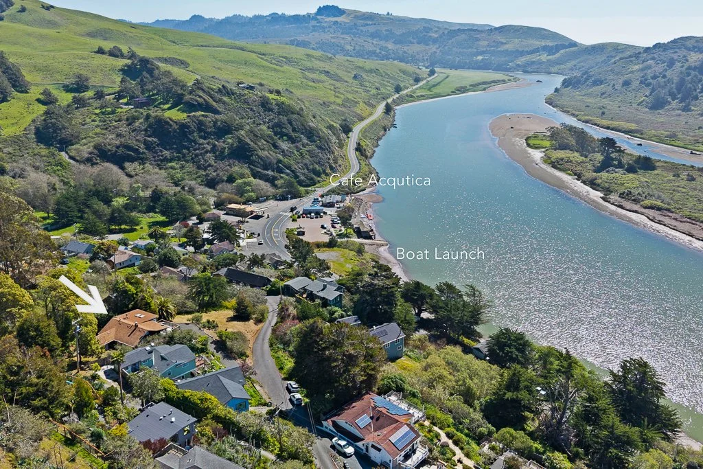 Aerial view of a river with hills on both sides, a small community with houses and a parking lot near the water, labeled spots for Cafe Acquatica and boat launch, surrounded by green vegetation.