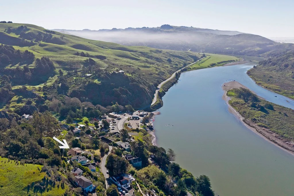 Aerial view of a winding river running through lush green hills with scattered houses and a small harbor on the riverbank.