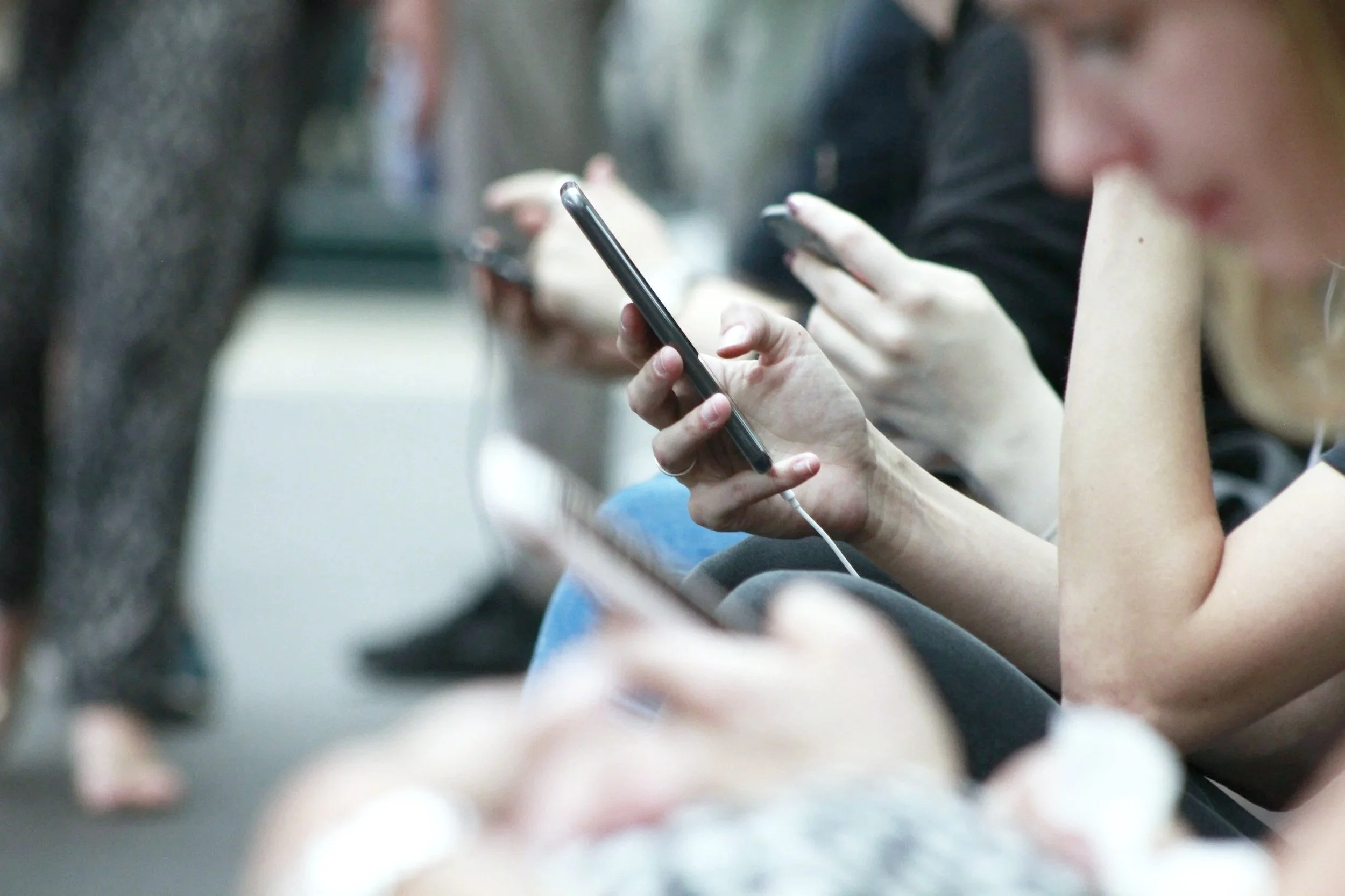 Menschen, die in einer Warteschlange sitzen und alle auf ihre Smartphones schauen.