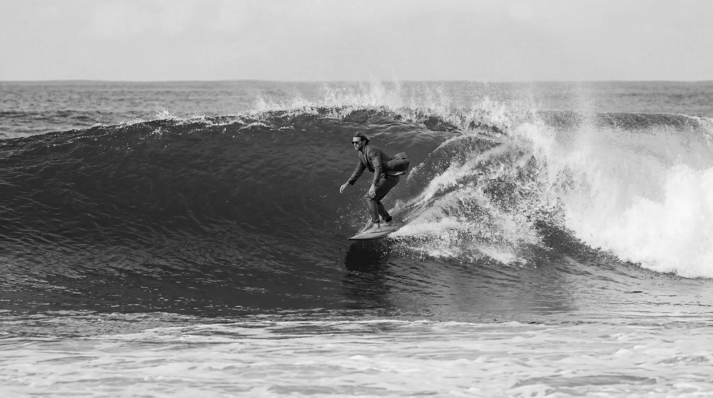 A person wearing sunglasses and a jacket surfing on a wave in the ocean.