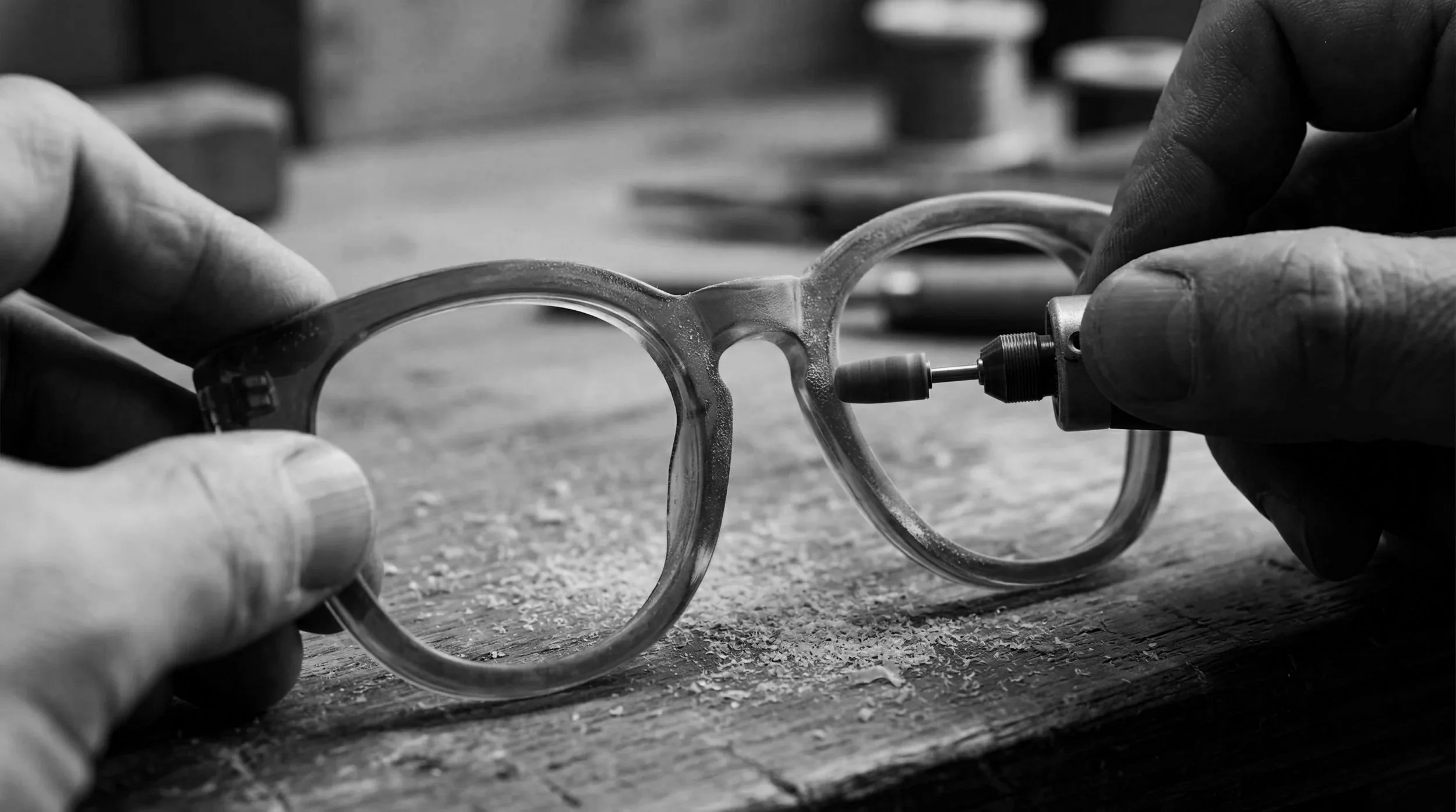 Person adjusting or repairing a pair of glasses with a small tool in a woodworking or craftsmanship workspace.