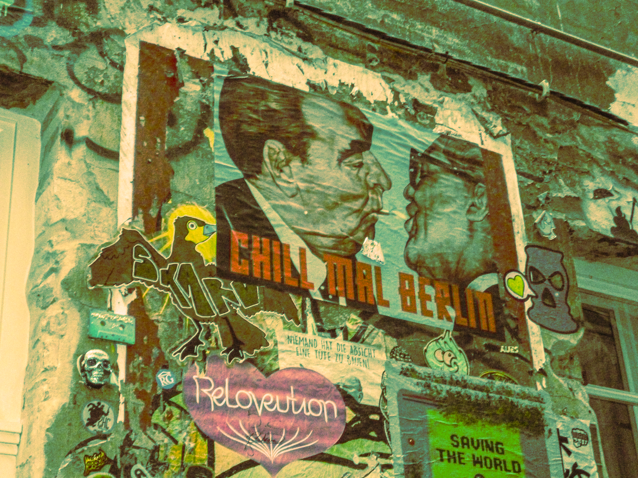 Wall with graffiti art including portraits of two men in profile, one with glasses and the other with a cigarette, a colorful bird, a skull, a heart with the words 'Relovution', and text in German about advocating for a utopian future. There are vari