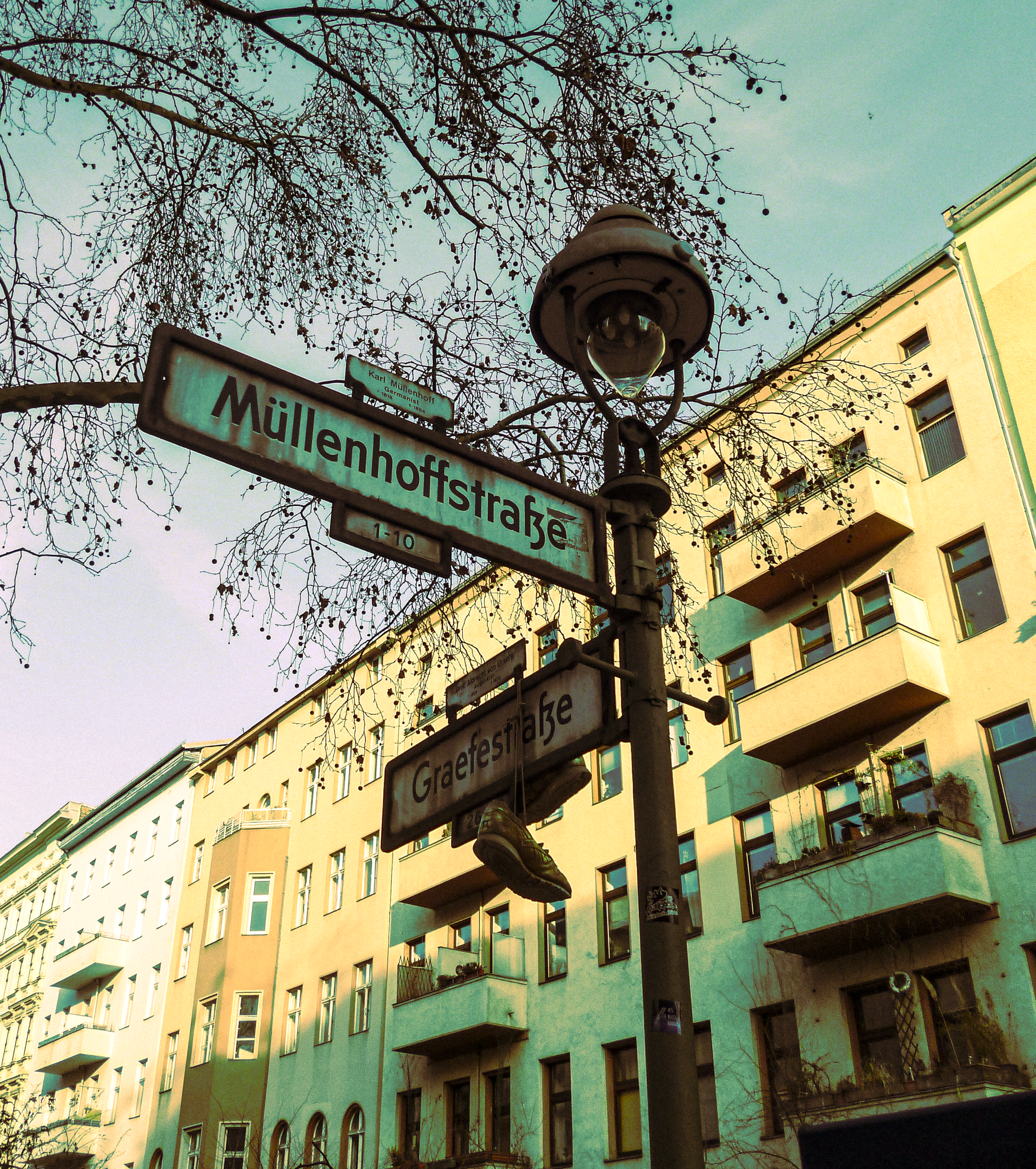 Street signs at the intersection of Mullenhoffstraße and Graefestraße in a city, with a building in the background and a streetlamp overhead.
