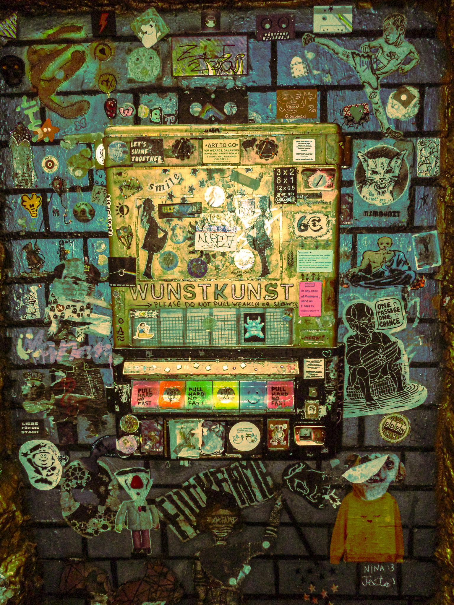 Colorful graffiti and stickers on a brick wall featuring drawings of people, animals, and abstract designs surrounding a vending machine with stickers and handwritten notes.