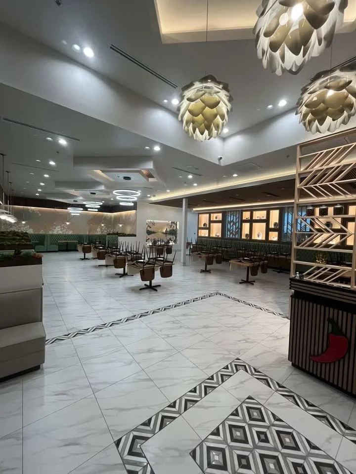 Empty dining or lounge area with modern lighting fixtures, patterned tile floors, and a variety of chairs and tables.