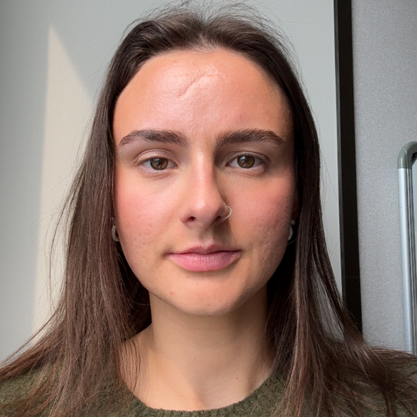 A young woman with long brown hair, light skin, and a nose ring, looking directly at the camera with a neutral expression.