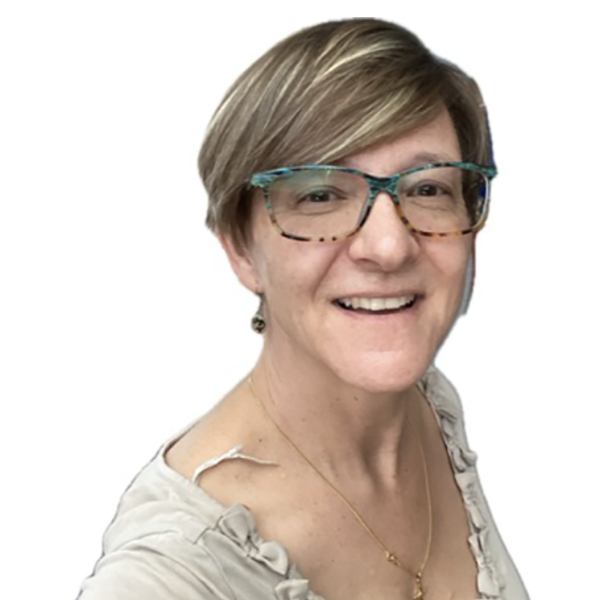 Smiling woman with short blonde hair, wearing glasses with a colorful frame, a beige top with ruffle details, and a gold necklace.