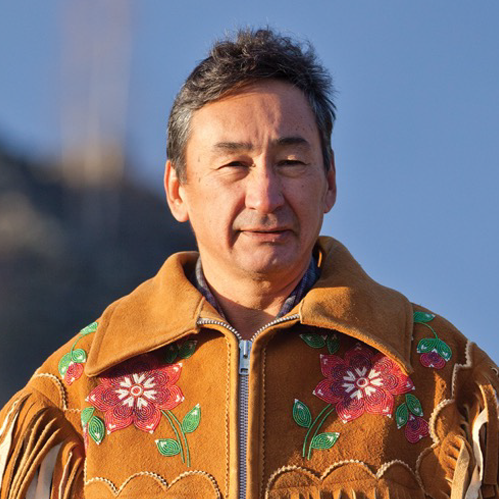 A man outdoors wearing a brown leather jacket with colorful floral embroidery.