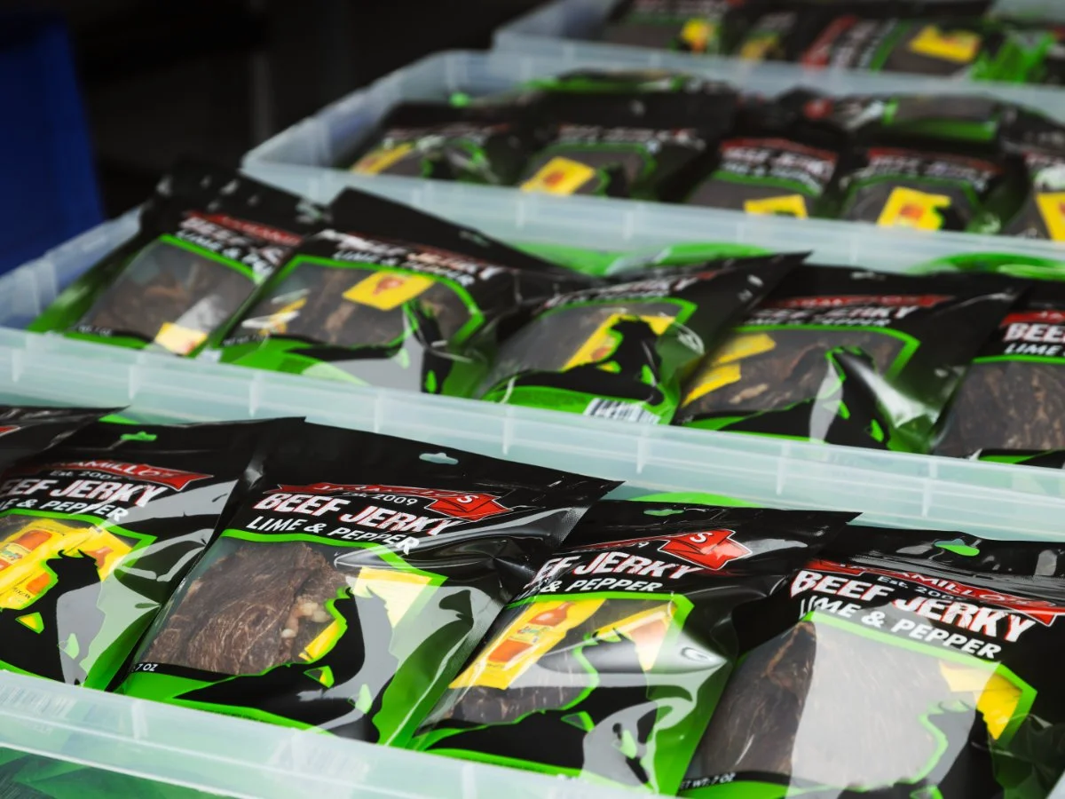 Bags of beef jerky with lime and pepper flavor stacked in a storage bin.