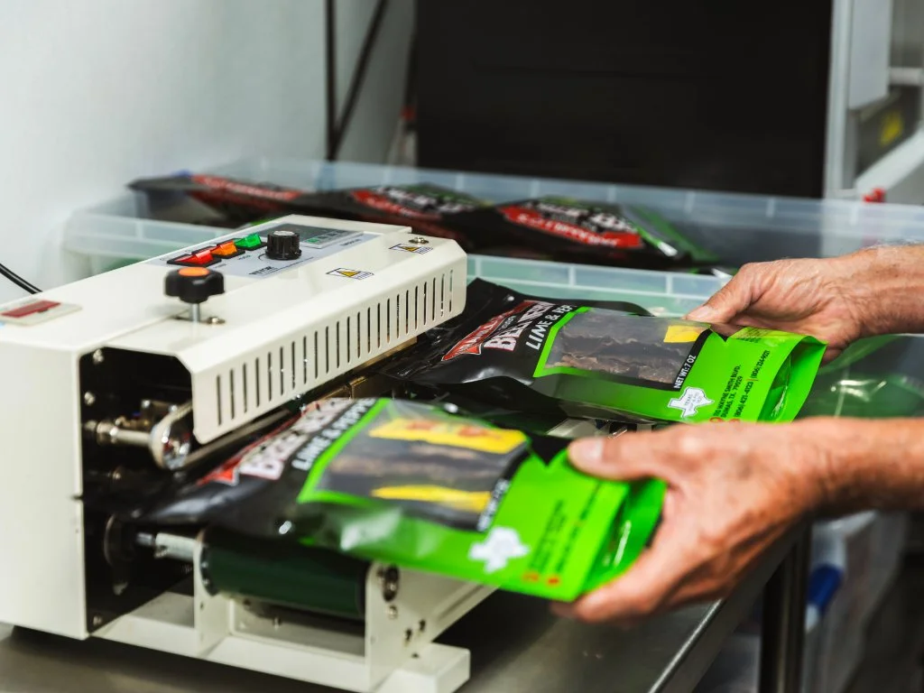 Person packaging bacon strips into green resealable bags using a machine.