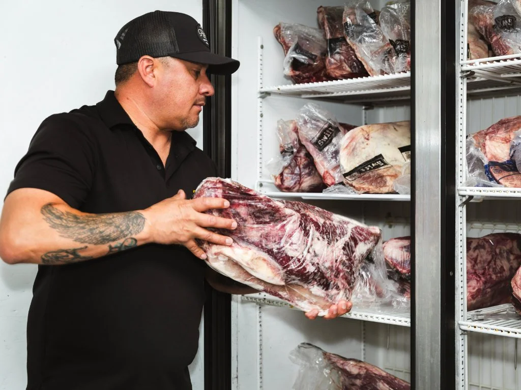 Man in black shirt and hat handling a large cut of frozen beef in a meat freezer