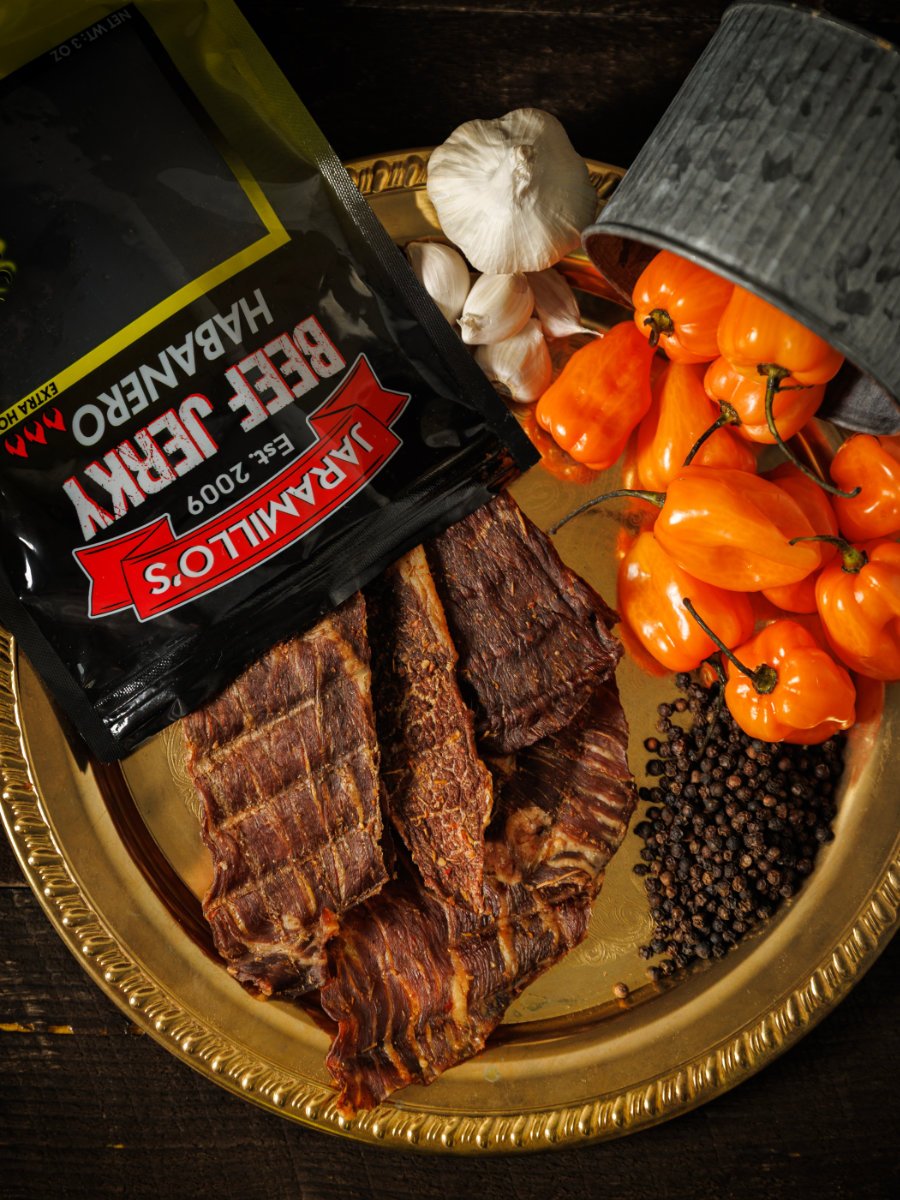 A gold tray containing smoked ribs, a bag of Jack Daniel's barbecue sauce, garlic bulbs, orange habanero peppers, and black peppercorns.