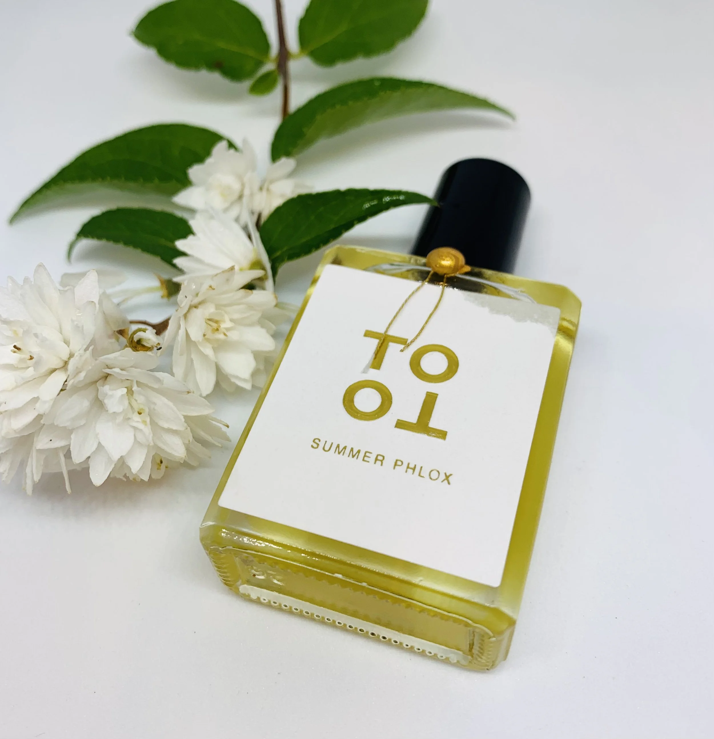 A perfume bottle labeled 'Summer Phlox' with white flowers and green leaves in the background.
