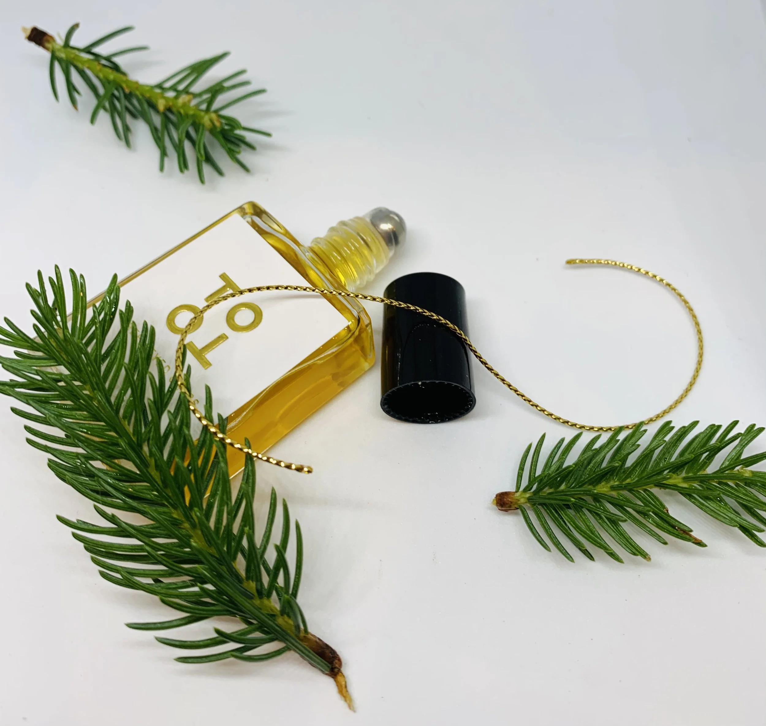 Assorted perfume bottles with pine branches on a white surface.