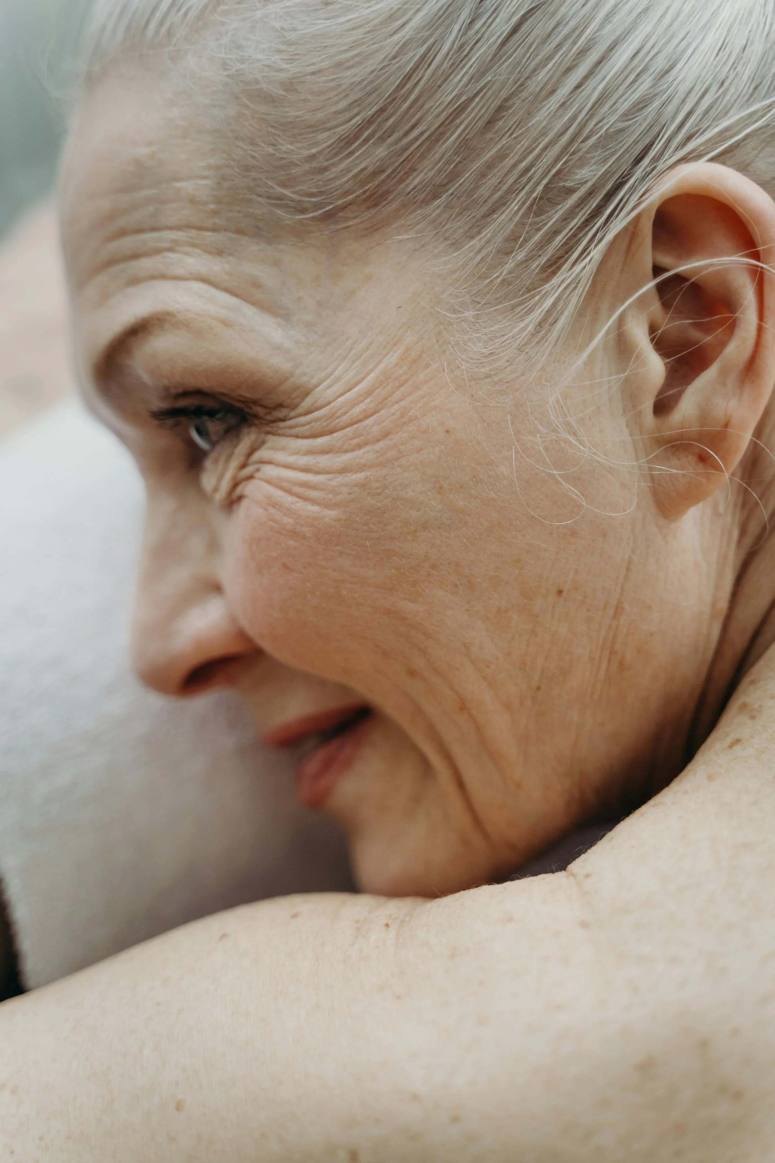 A close-up side view of an elderly woman's face, showing her smiling with her eyes closed, emphasizing her wrinkles and silver hair.