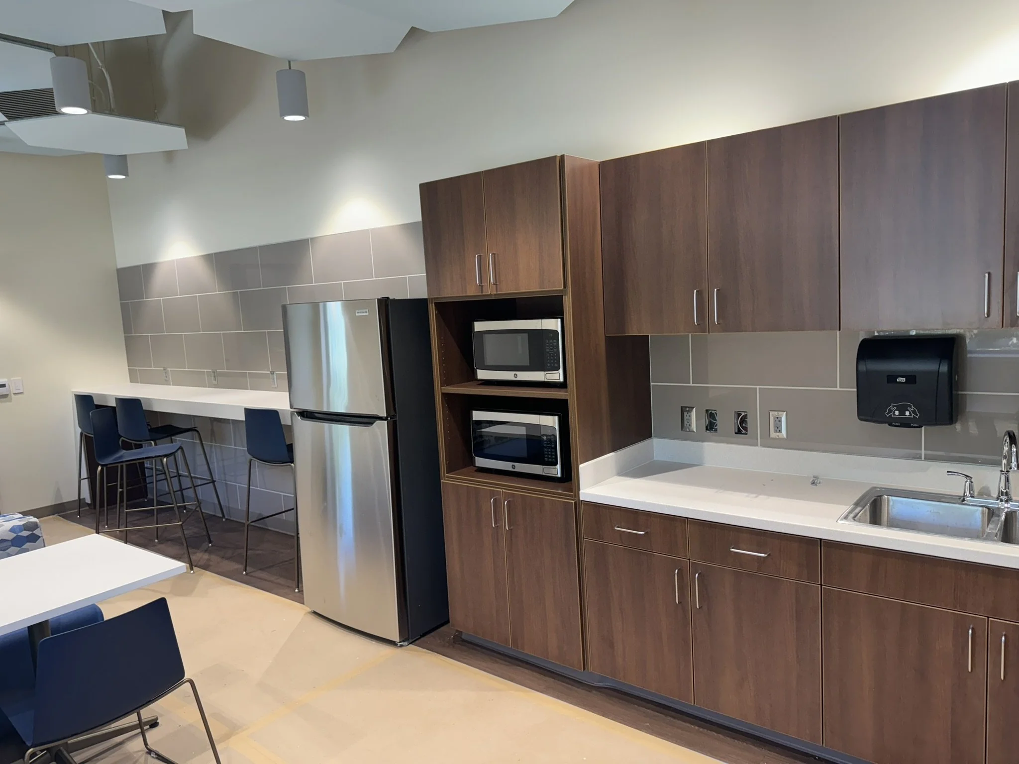 Kitchen with brown cabinets, a microwave, a refrigerator, a sink, and modern hanging light fixtures.