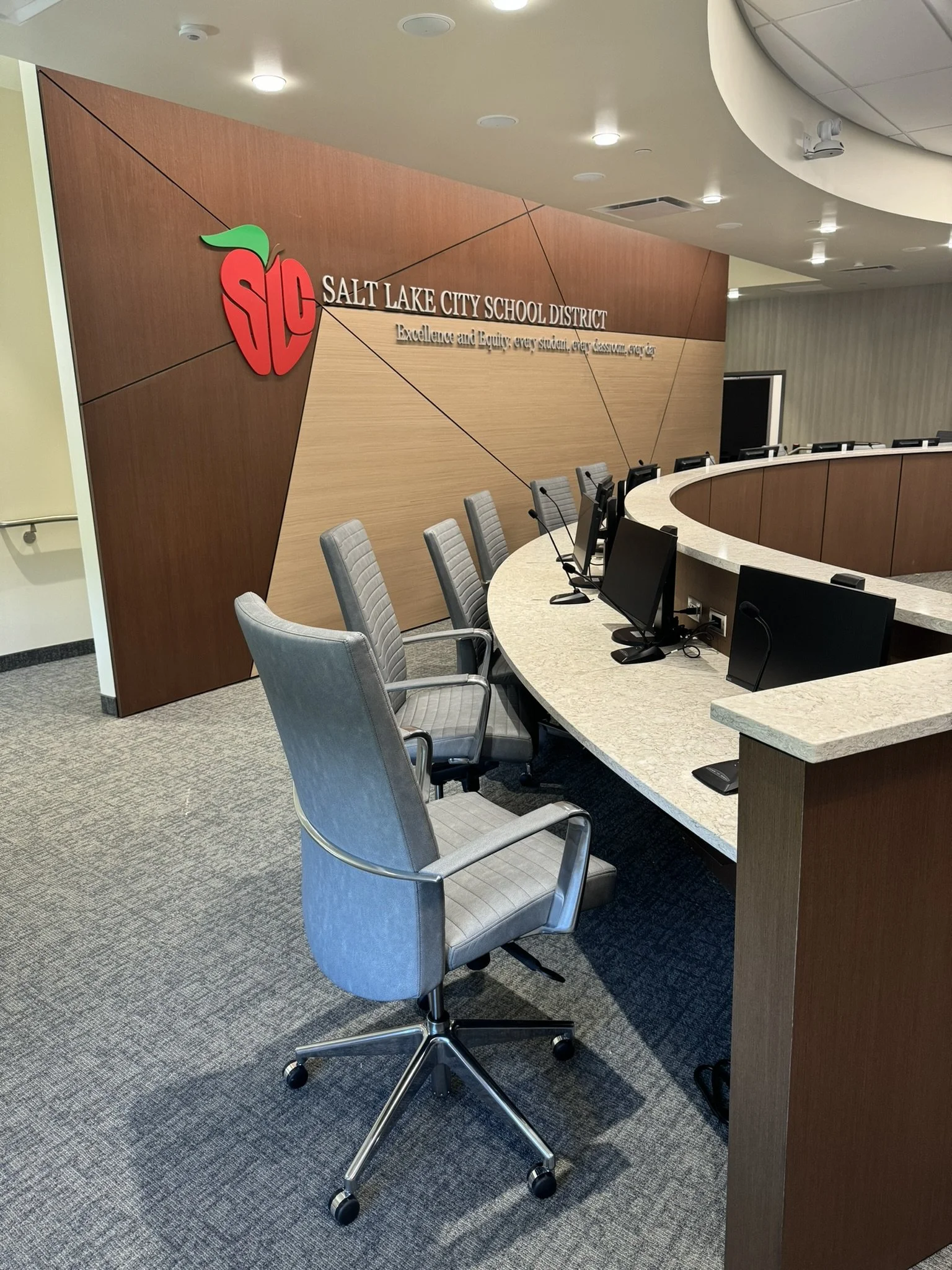View of the reception or conference room area of Salt Lake City School District with a curved desk, chairs, and a wall sign with the district's logo and slogan.