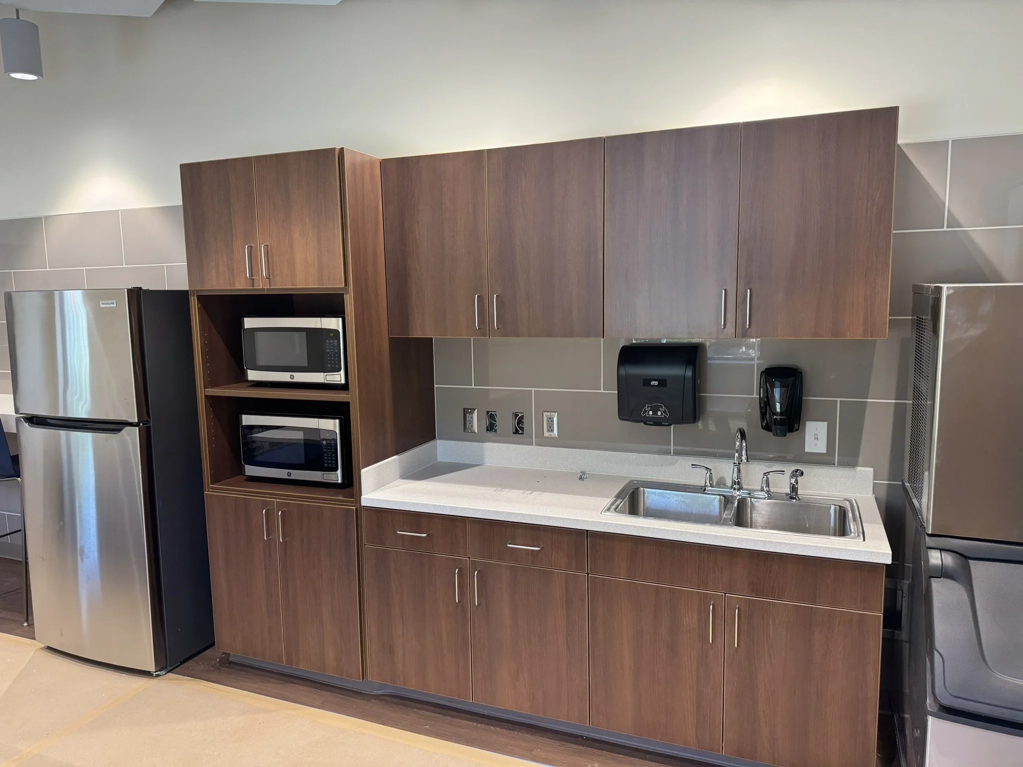 Kitchen area with wooden cabinets, stainless steel refrigerator, microwave, and countertop with sink.