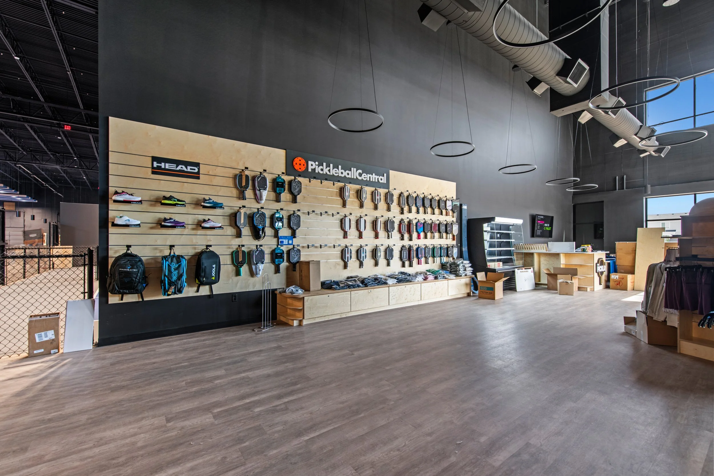 An indoor sports shop with tennis and pickleball equipment, including shoes, paddles, and bags, with a large sign reading 'Pickleball Central' and 'HEAD'.