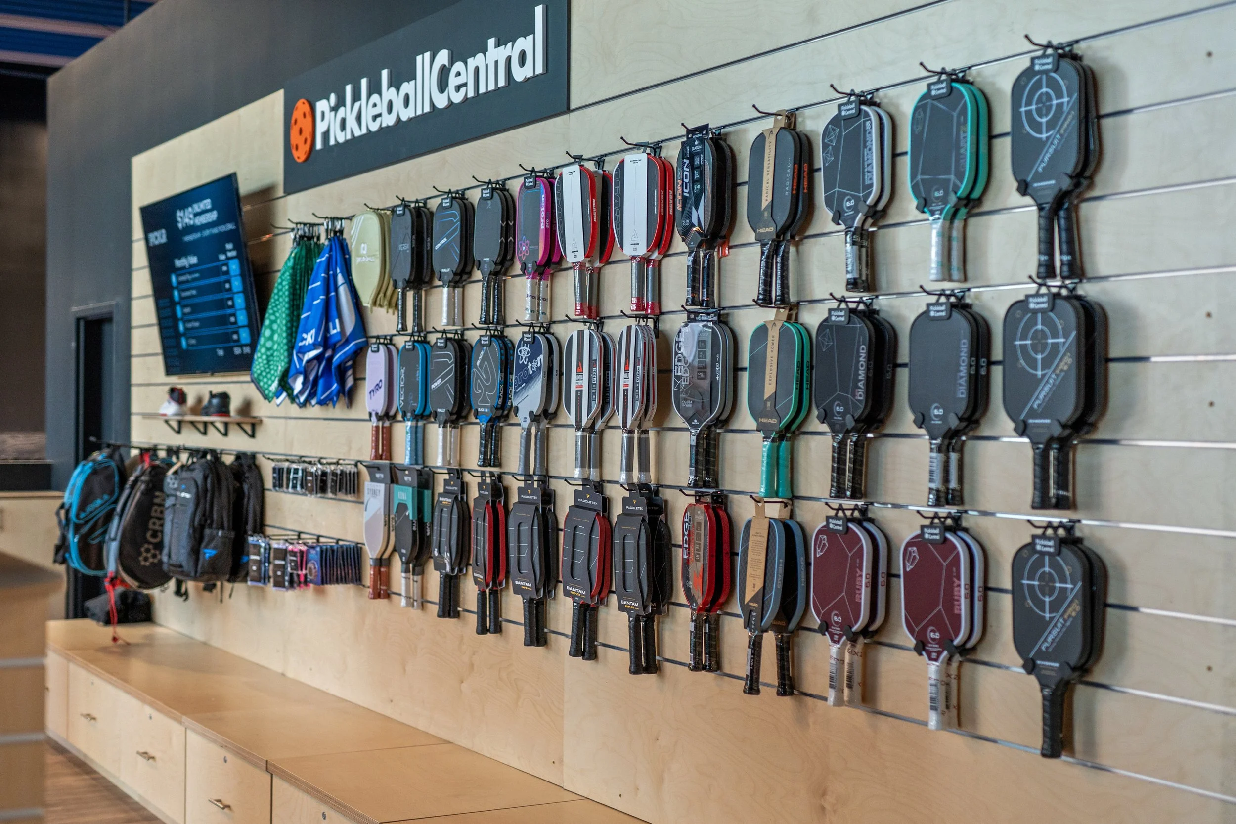Display of pickleball paddles hanging on a wall at Pickleball Central with a sign above.