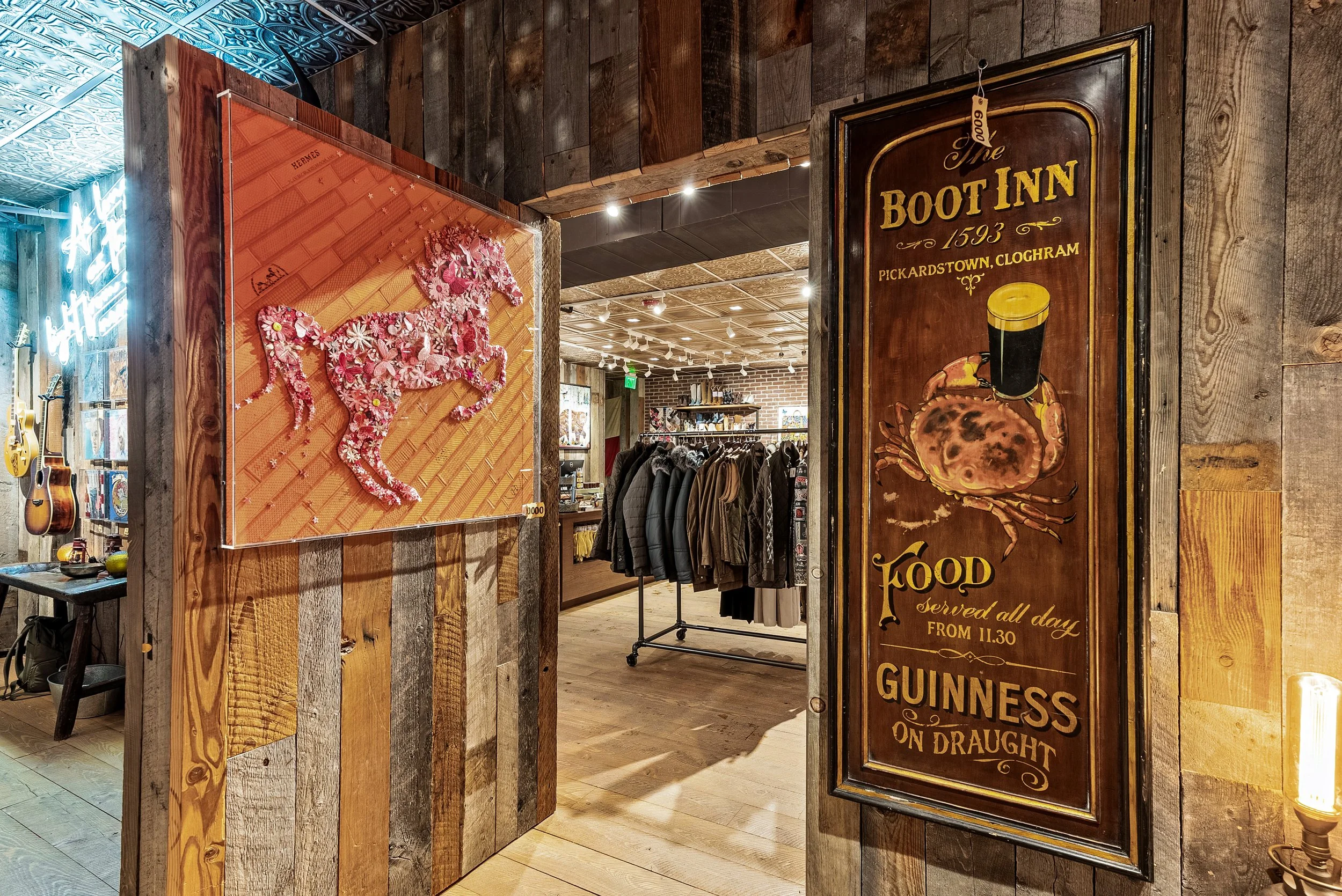 Interior of a store with wooden walls, displaying artwork, signs, and clothing racks. A decorated horse art piece and a Guinness sign are visible.