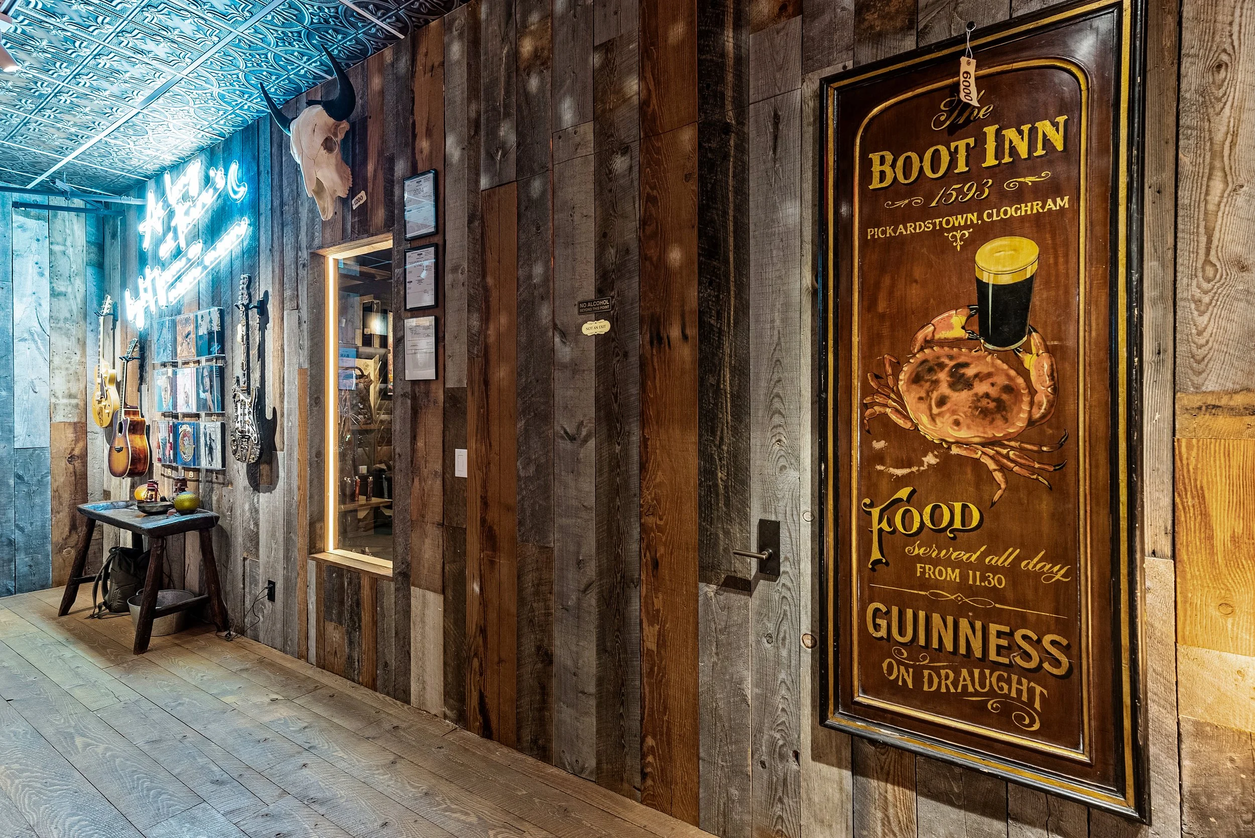 Decorative interior of a pub or restaurant with wood-paneled walls, a neon sign, hanging animal skull, framed certificates, guitar artwork, and a large Guinness poster featuring a crab and a pint of beer.