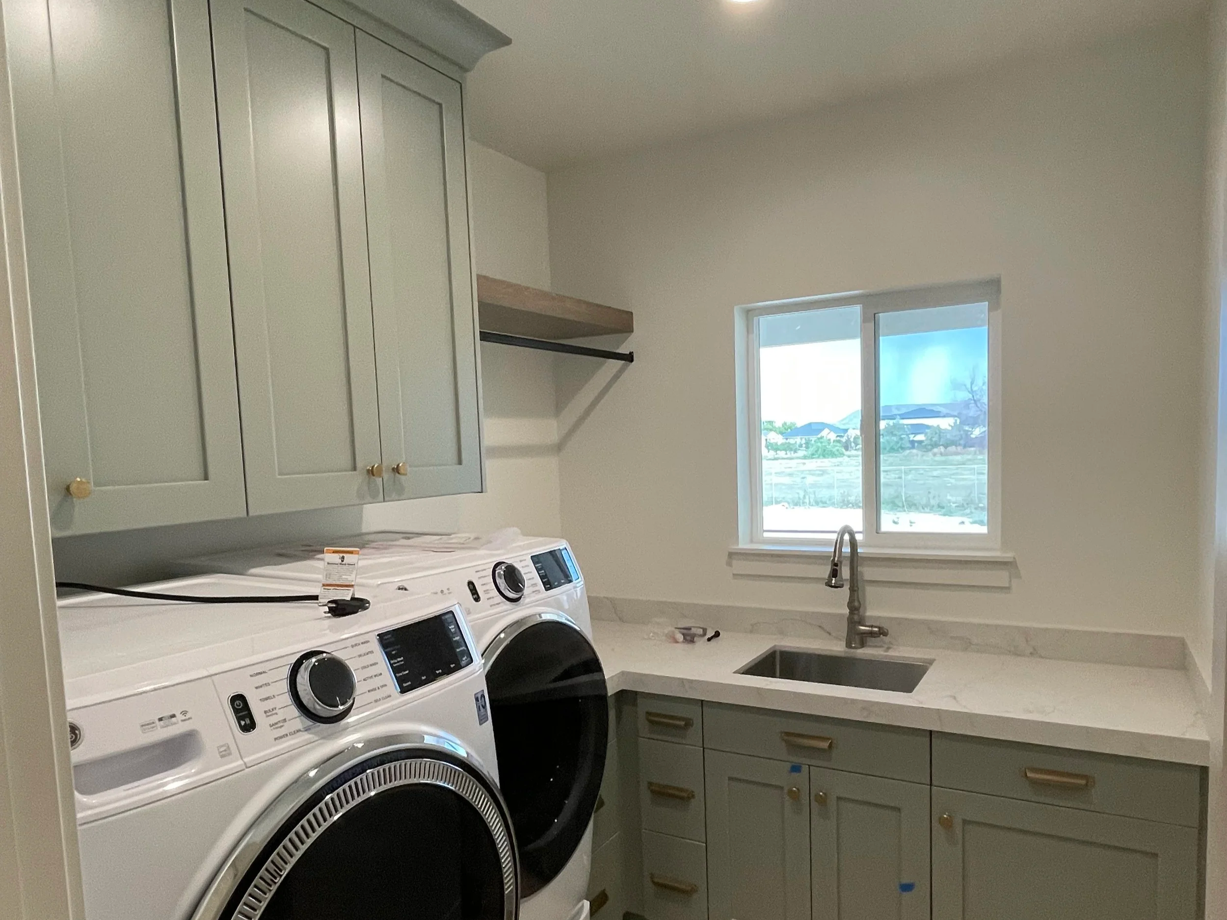 A laundry room with a white washing machine and dryer, green cabinets, a window, and a sink.