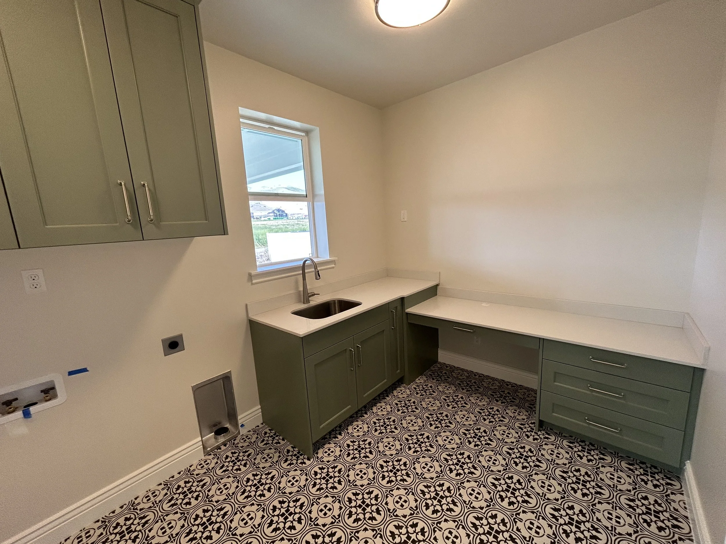 Kitchen with green cabinets, a window above the sink, a decorative patterned floor, and empty walls.