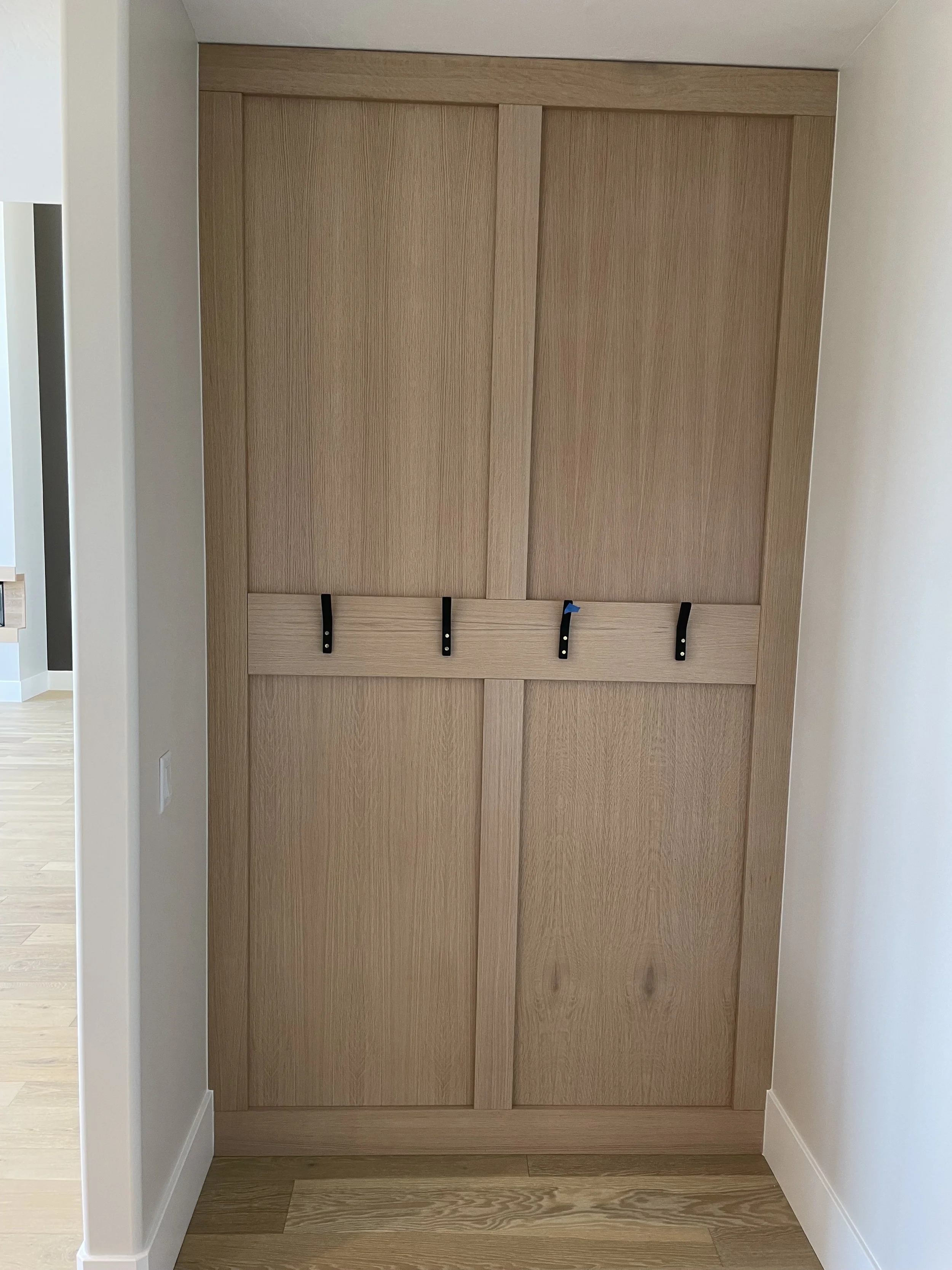 Wooden closet with four black hooks hanging on a horizontal rail inside a room with white walls and wood flooring.