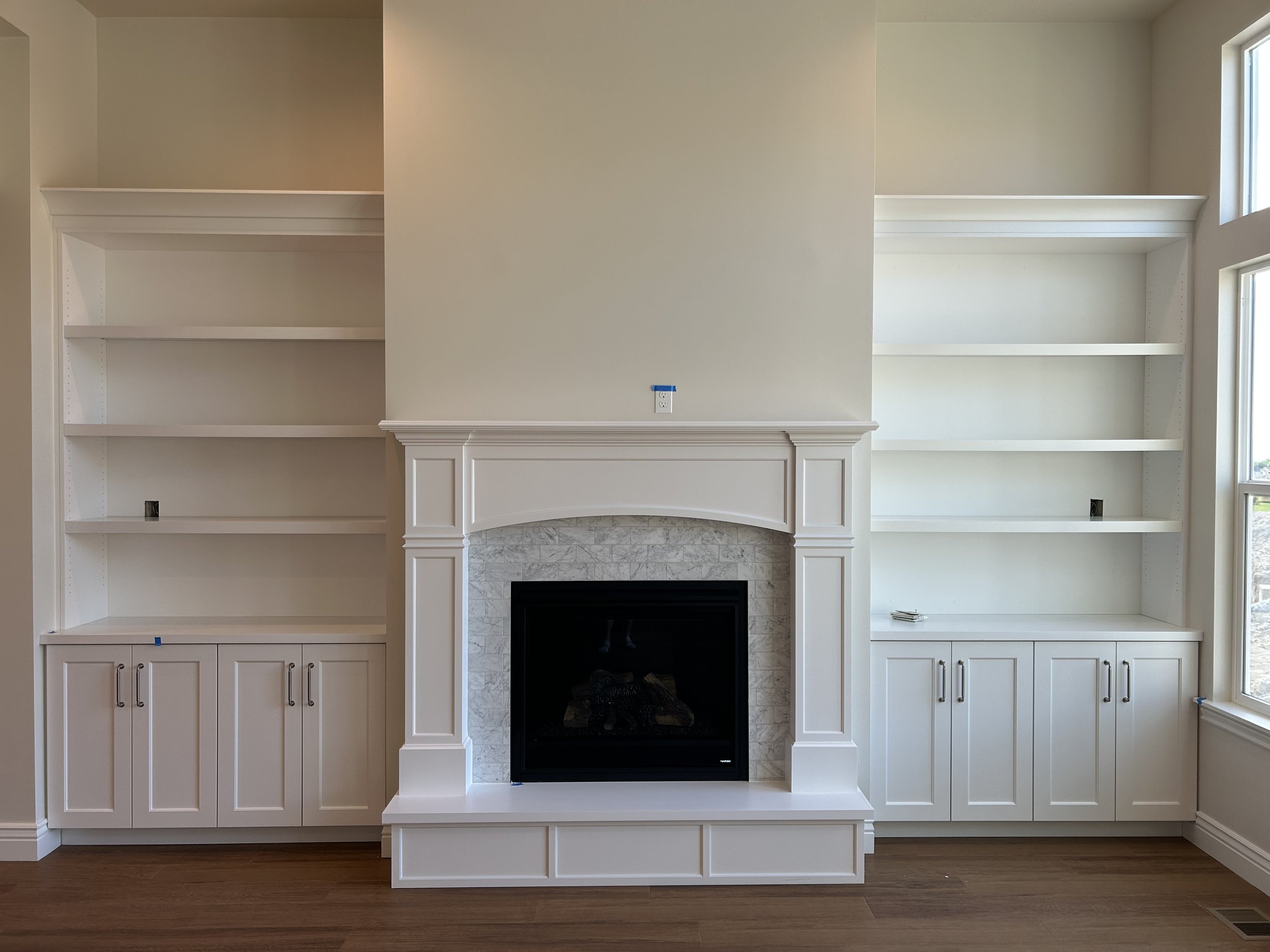Empty white built-in bookshelves flanking a fireplace with tile surround, in a room under construction or renovation.