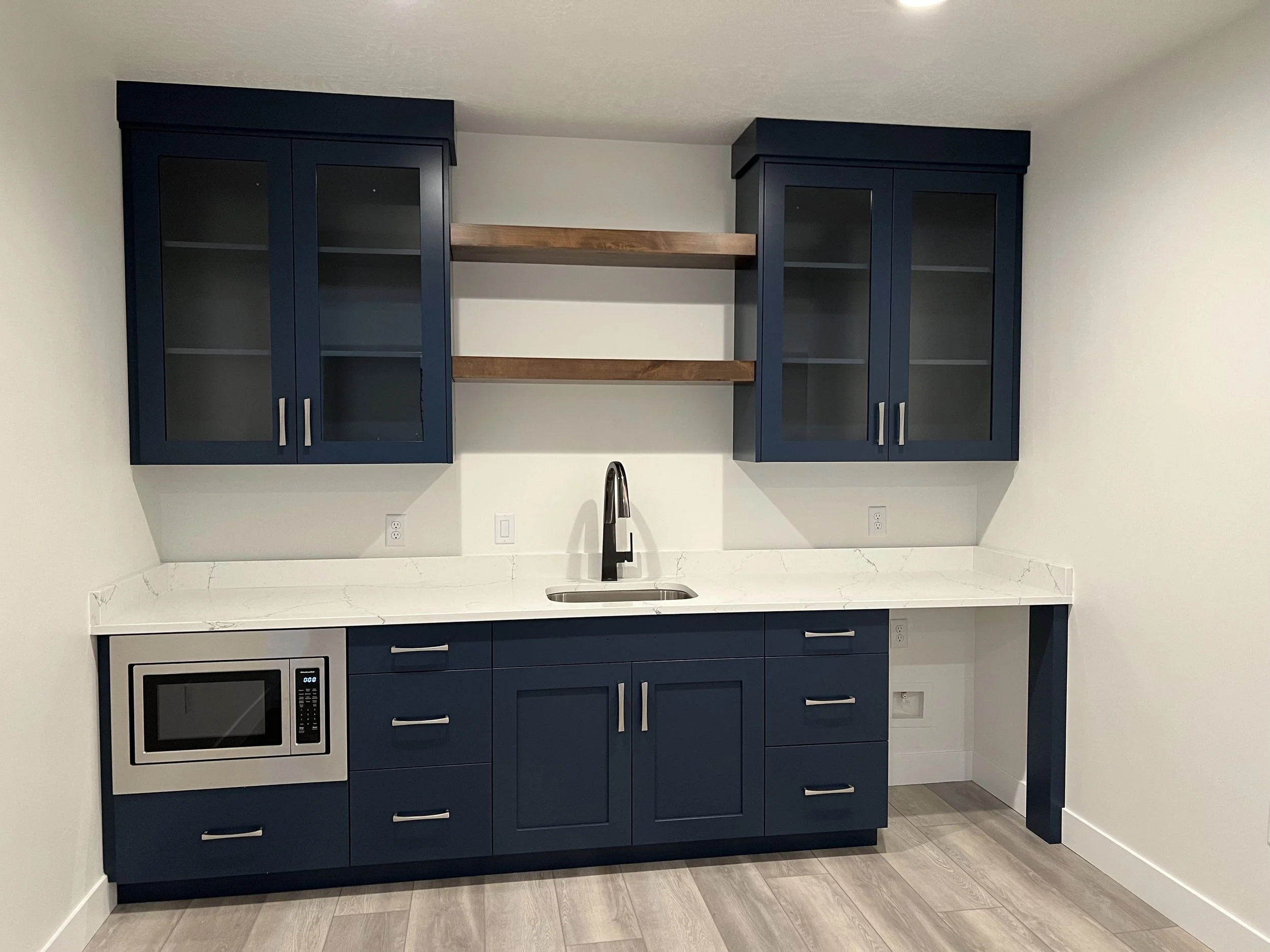 Modern kitchen with navy blue cabinets, white marble countertop, stainless steel microwave, and a kitchen sink with a black faucet.