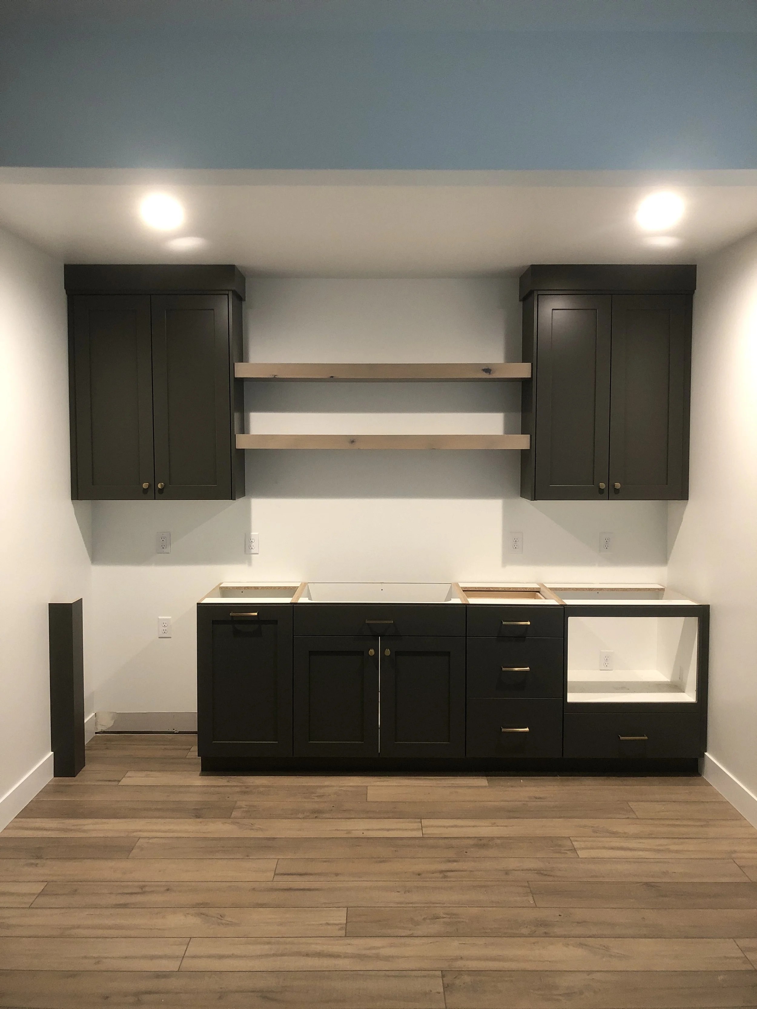 Room with built-in black kitchen cabinets, upper shelves, and wood flooring, no appliances or other furniture visible.
