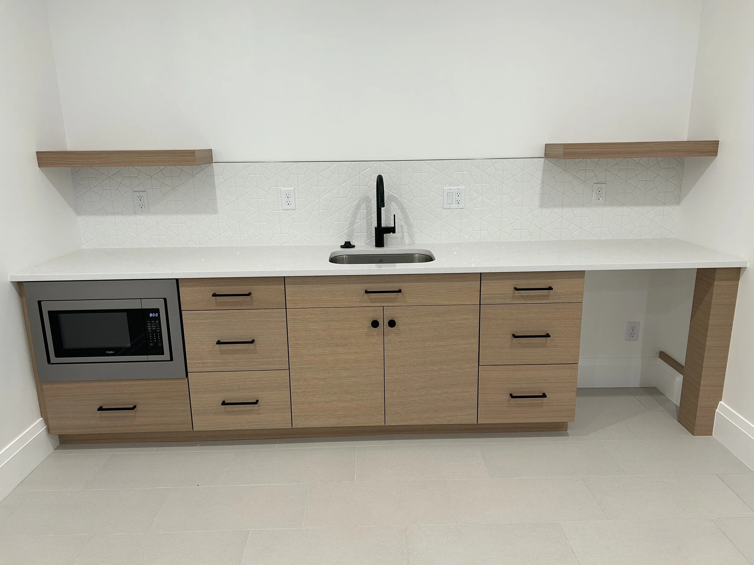 Modern kitchen with light wood cabinets, white countertop, black faucet, and a built-in microwave.