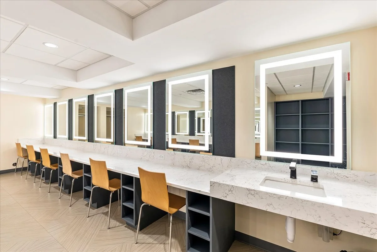 A row of wooden chairs in front of illuminated square mirrors above a white marble countertop in a modern salon or makeup station.