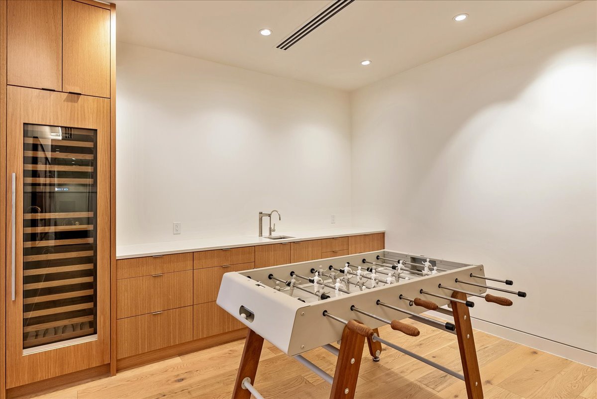 A room with a foosball table, wooden cabinetry, a wine cooler, a countertop with a sink, and ceiling lights.