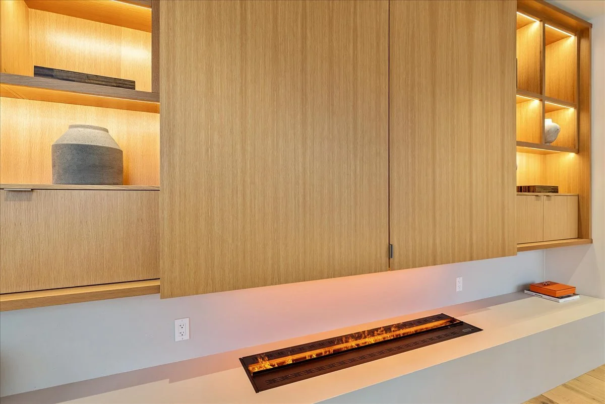 Wooden built-in shelves with decorative items, a fireplace with orange flames, and a white surface with books on it.