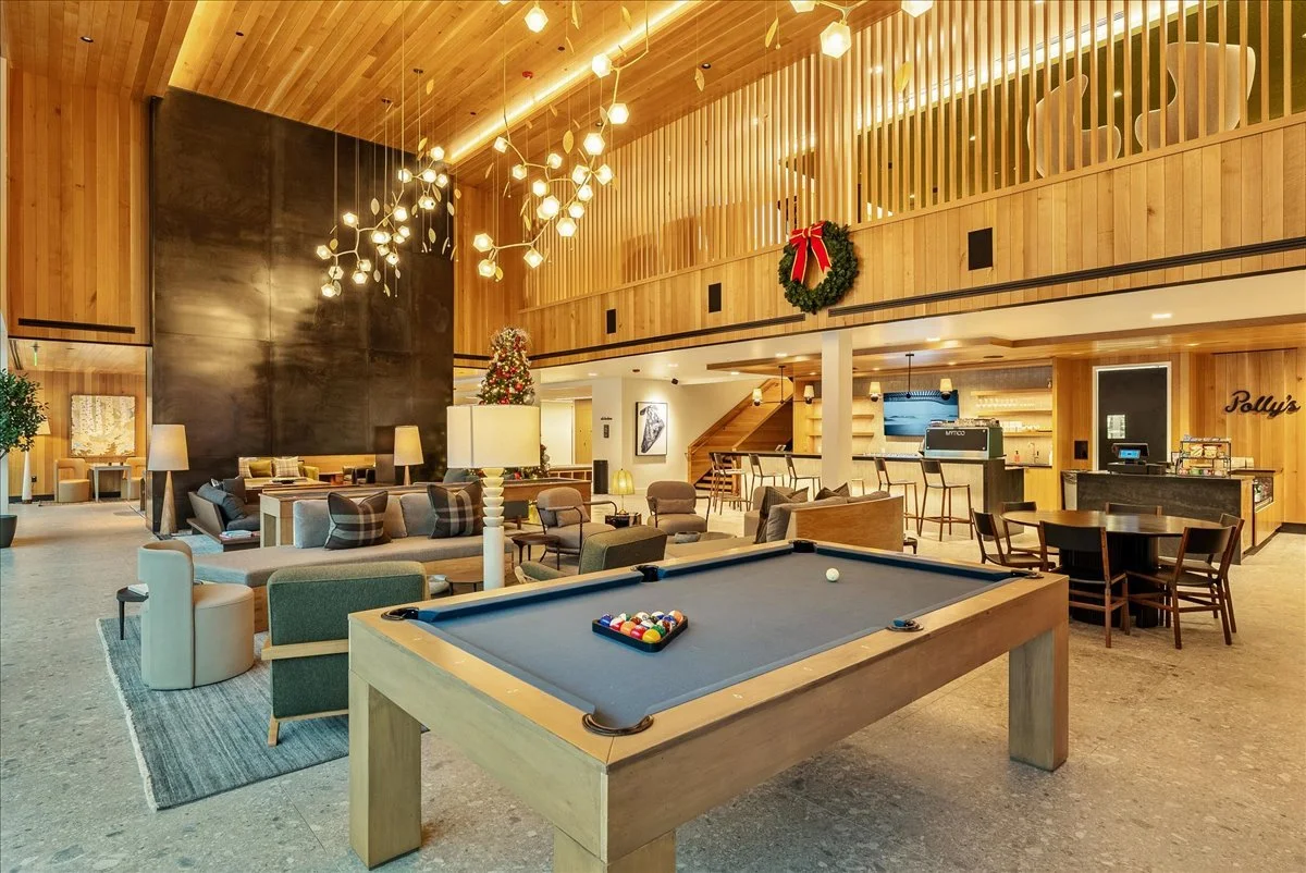 Hotel lobby decorated for Christmas with a pool table in the foreground, seating area with couches and lamps, a Christmas tree, and a bar area in the background.