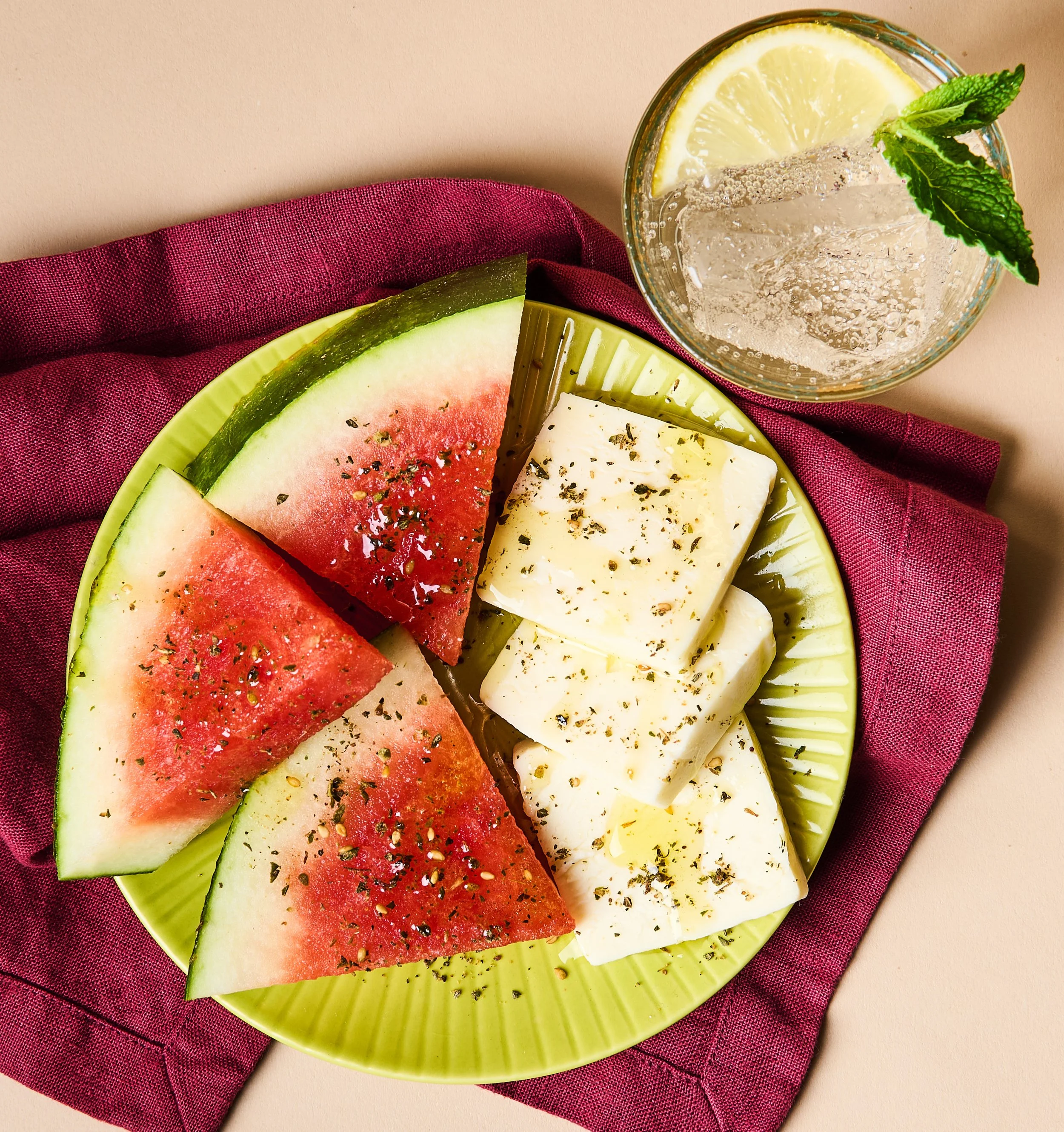 Sliced watermelon and cheese on a yellow plate, garnished with herbs, placed on a red cloth napkin.