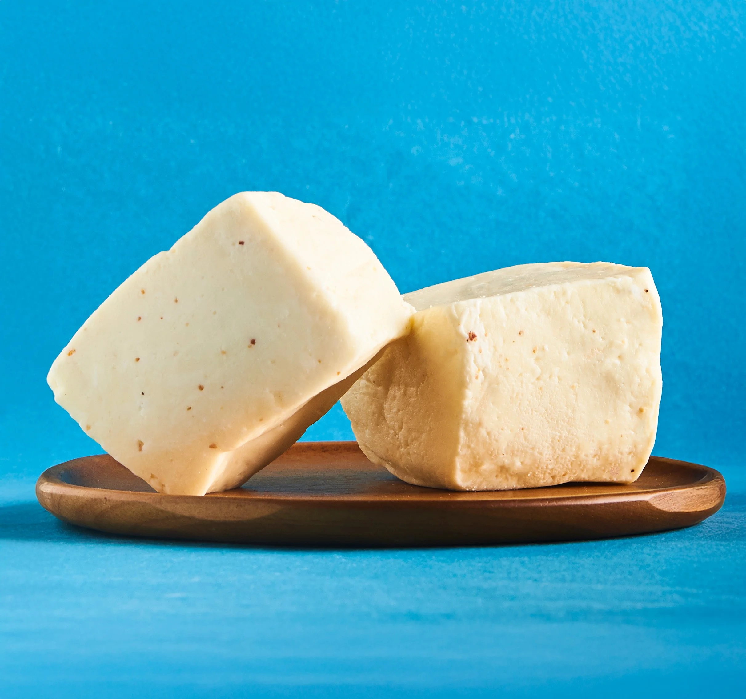 Close-up of sliced pieces of cheese on a wooden plate against a blue background.