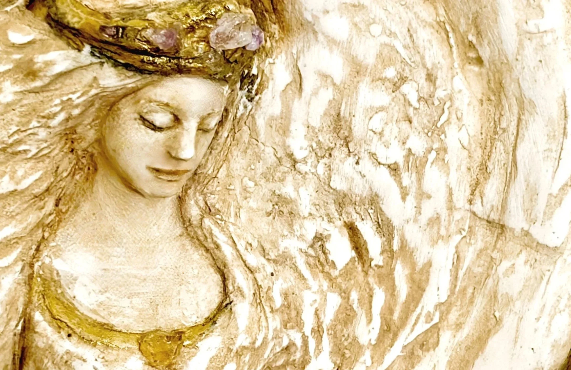 A golden-colored sculpture of a woman's face with closed eyes and flowing hair, set against a marbled background.