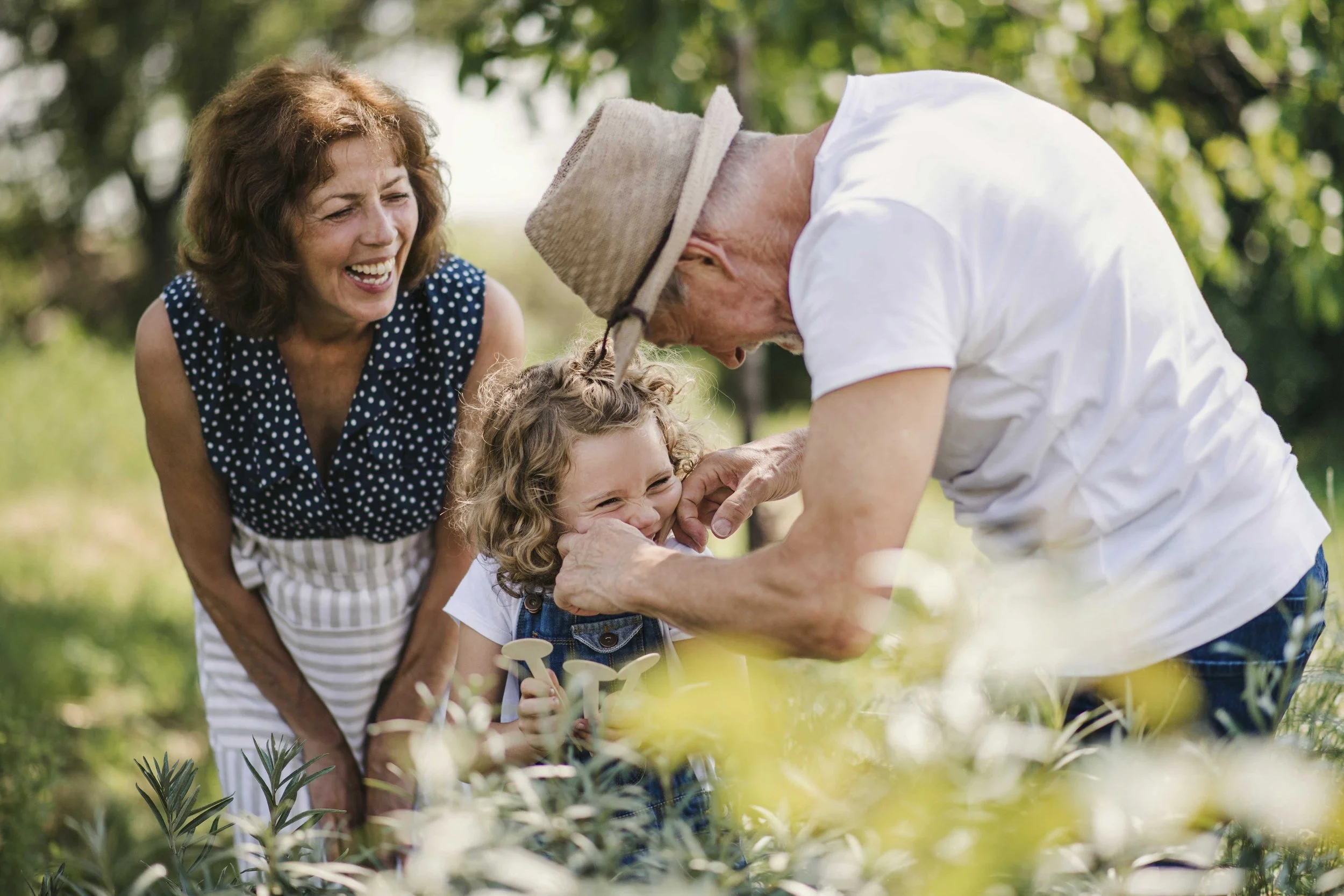 Grandparents playing with granddaughter outdoors in a garden.