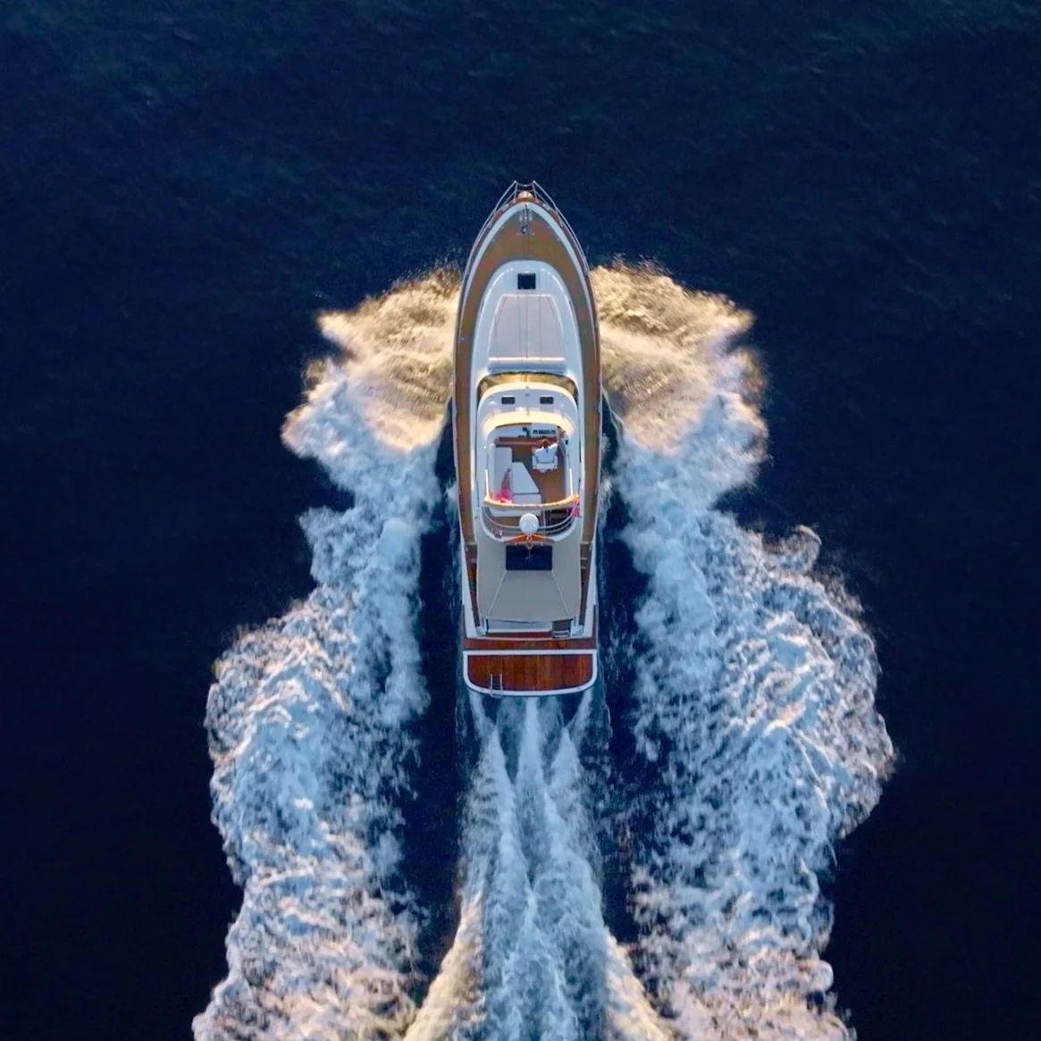 Aerial view of a motor yacht moving through dark blue water, creating white wake and splashes.