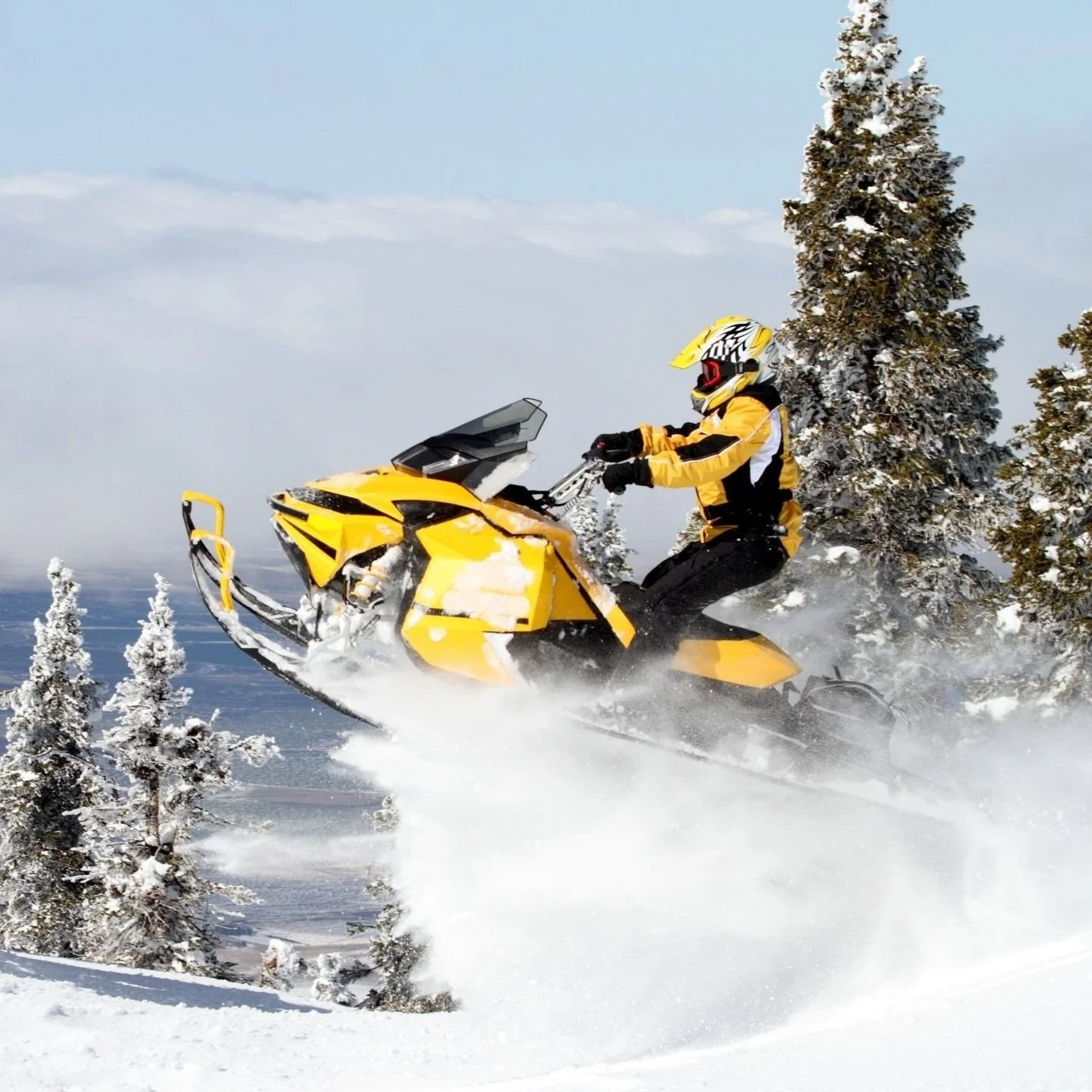 A person riding a yellow snowmobile through snow-covered trees in a winter landscape.