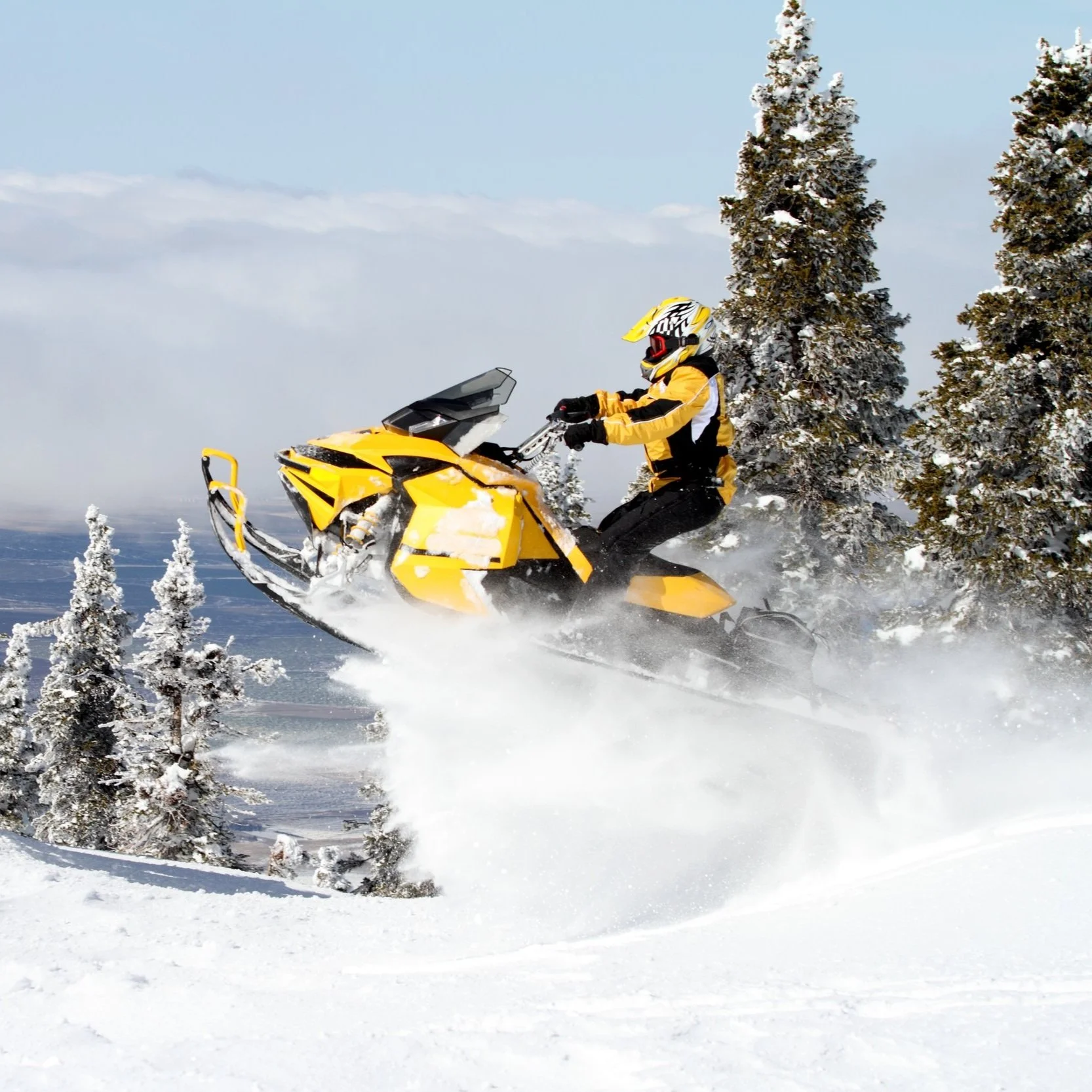 A person riding a yellow snowmobile through snowy trees during daytime.