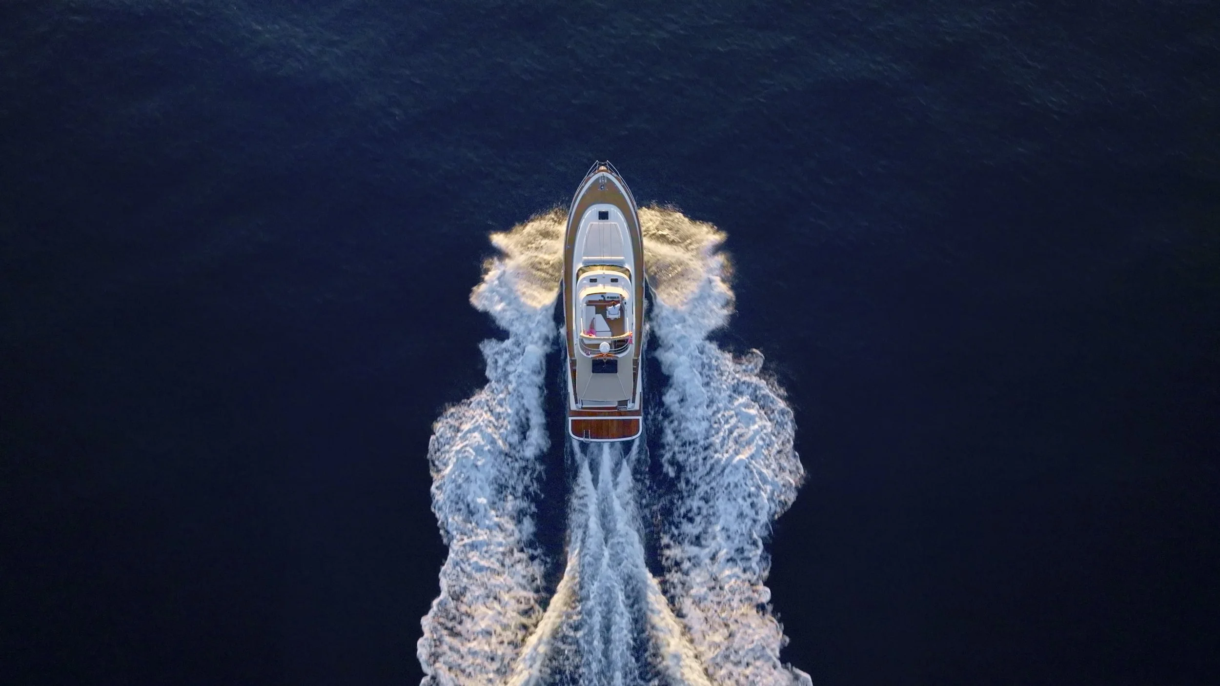An aerial view of a white yacht cruising on the open ocean, leaving a foamy wake behind it.