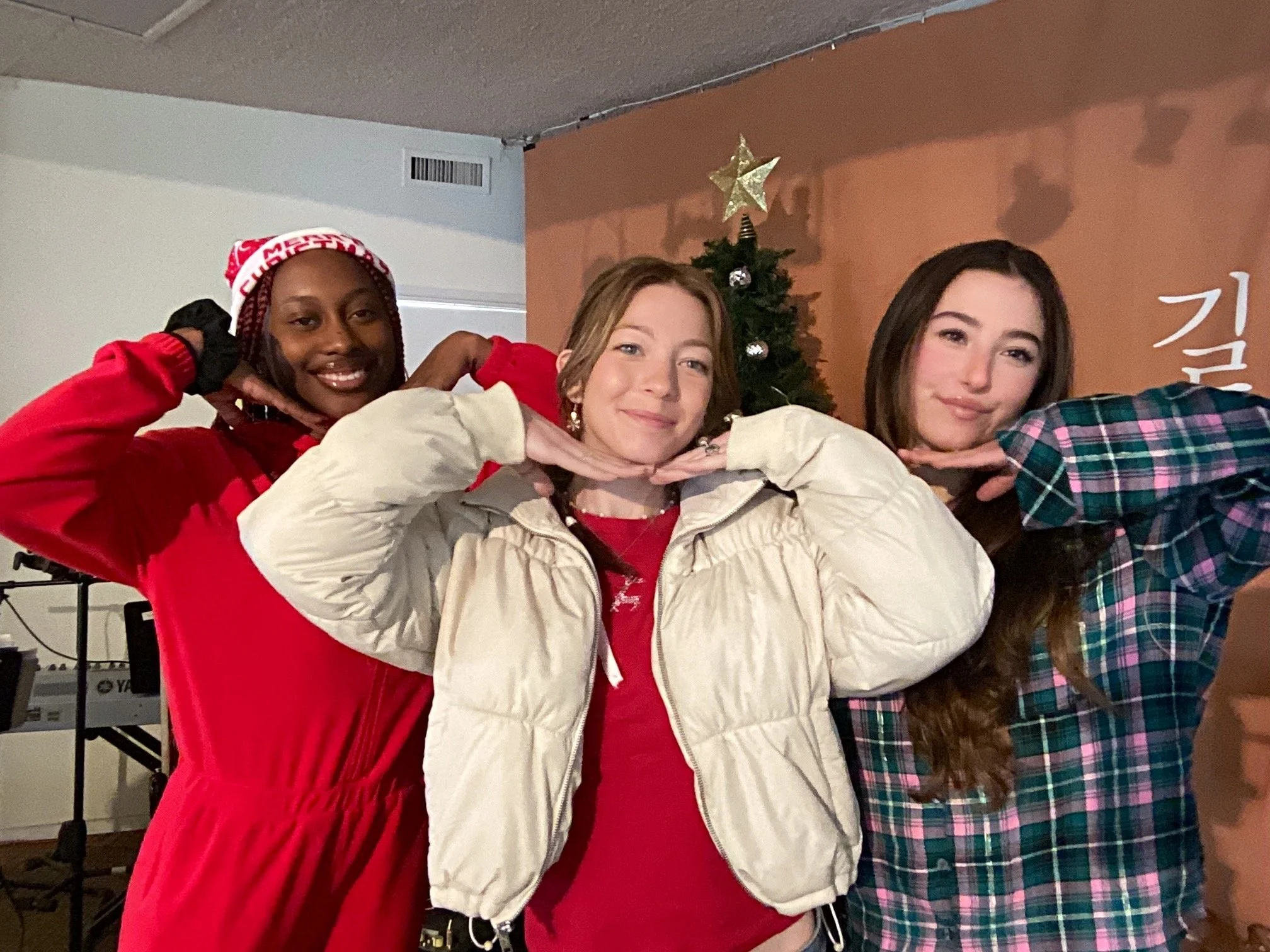 Three women posing with their hands under their chins in front of a decorated Christmas tree.