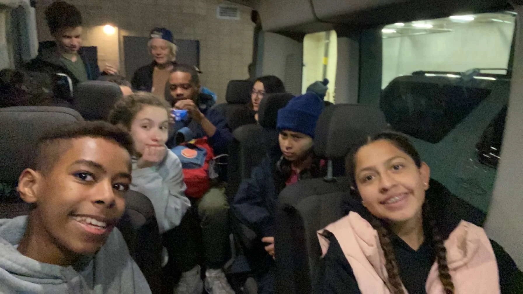 Group of children sitting in the back of a vehicle, smiling and posing for the camera, some wearing jackets and hats.