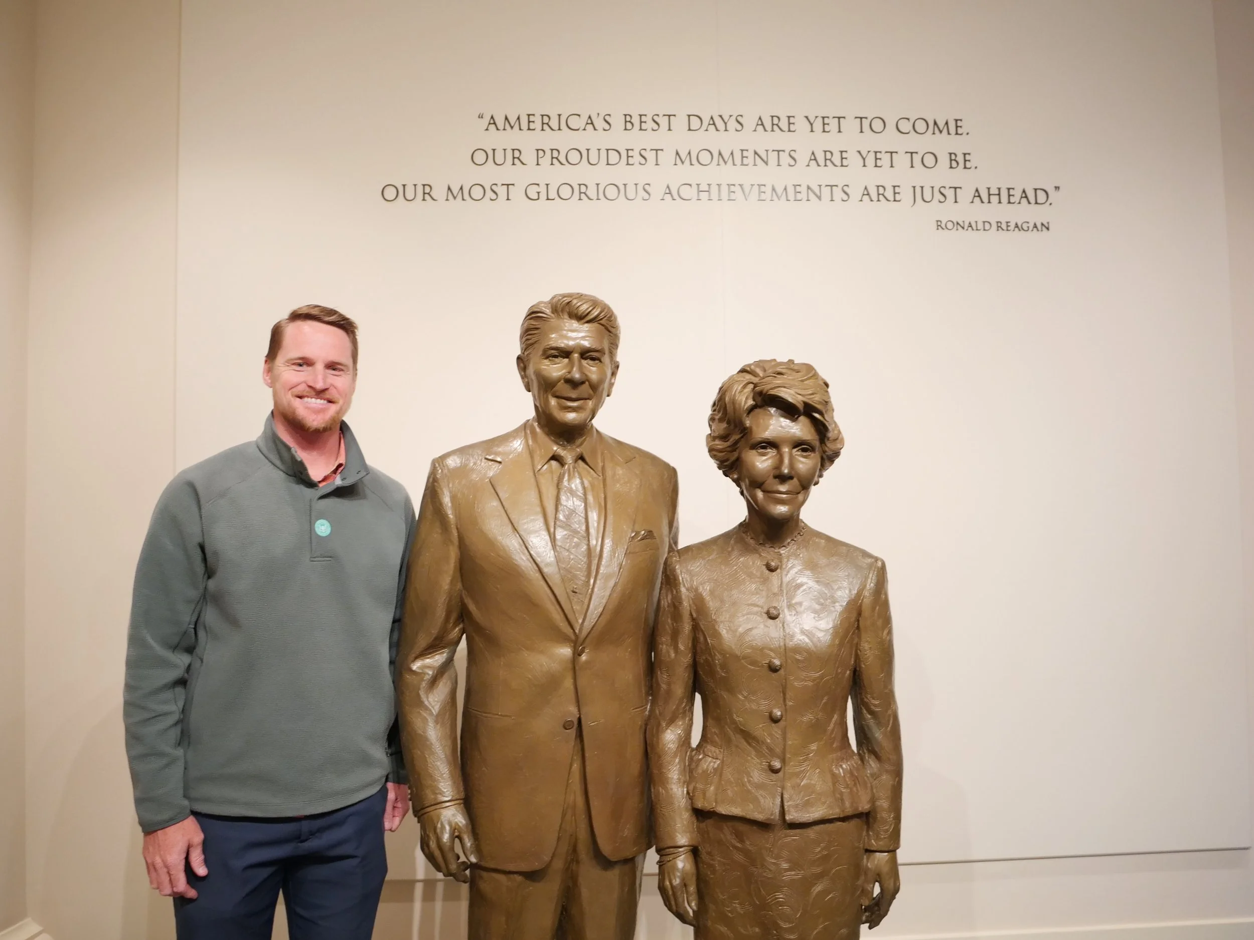 A man standing next to bronze statues of President Ronald Reagan and First Lady Nancy Reagan.